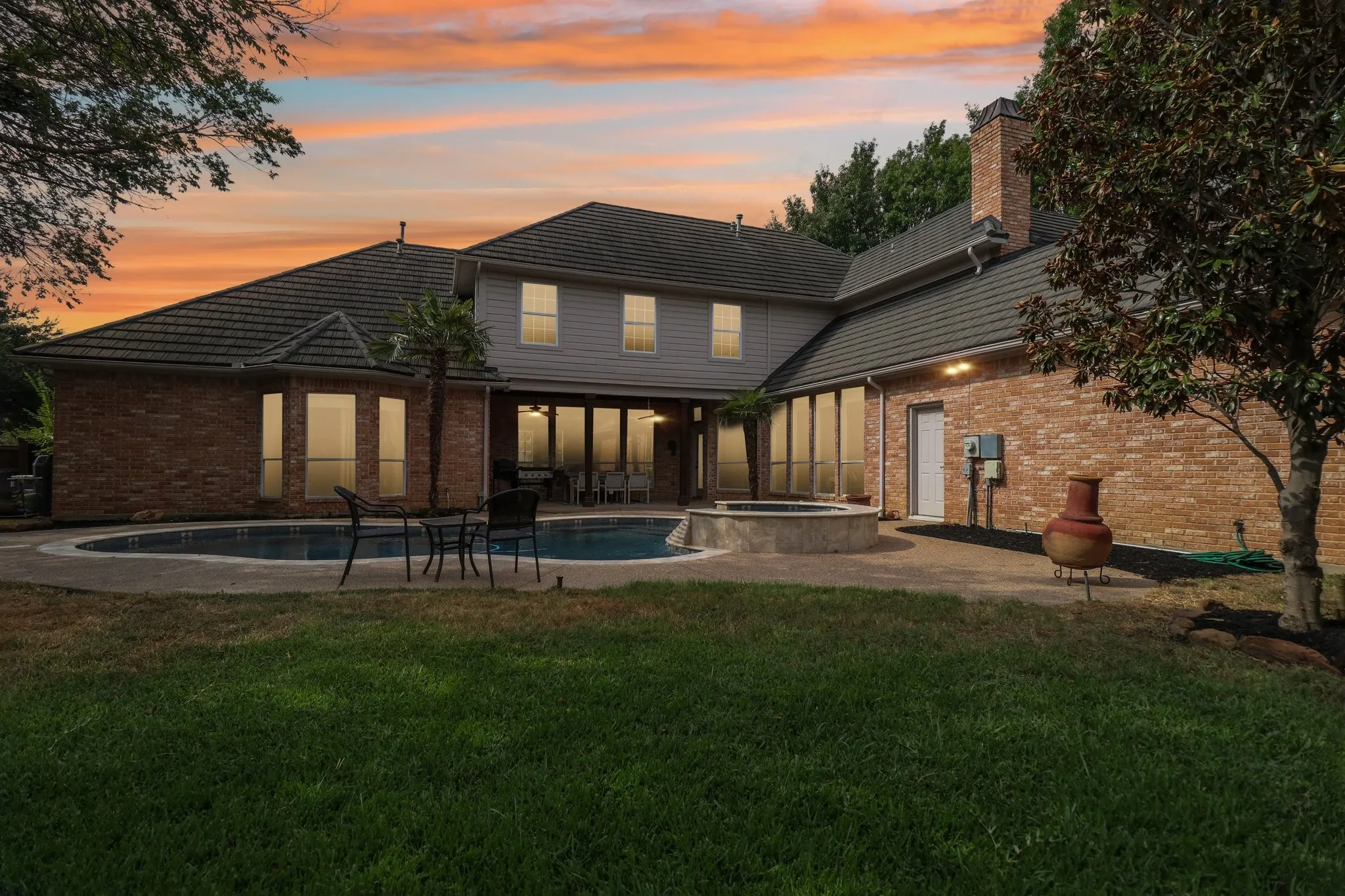 Expansive backyard featuring a curved swimming pool, integrated spa, and a brick-clad exterior