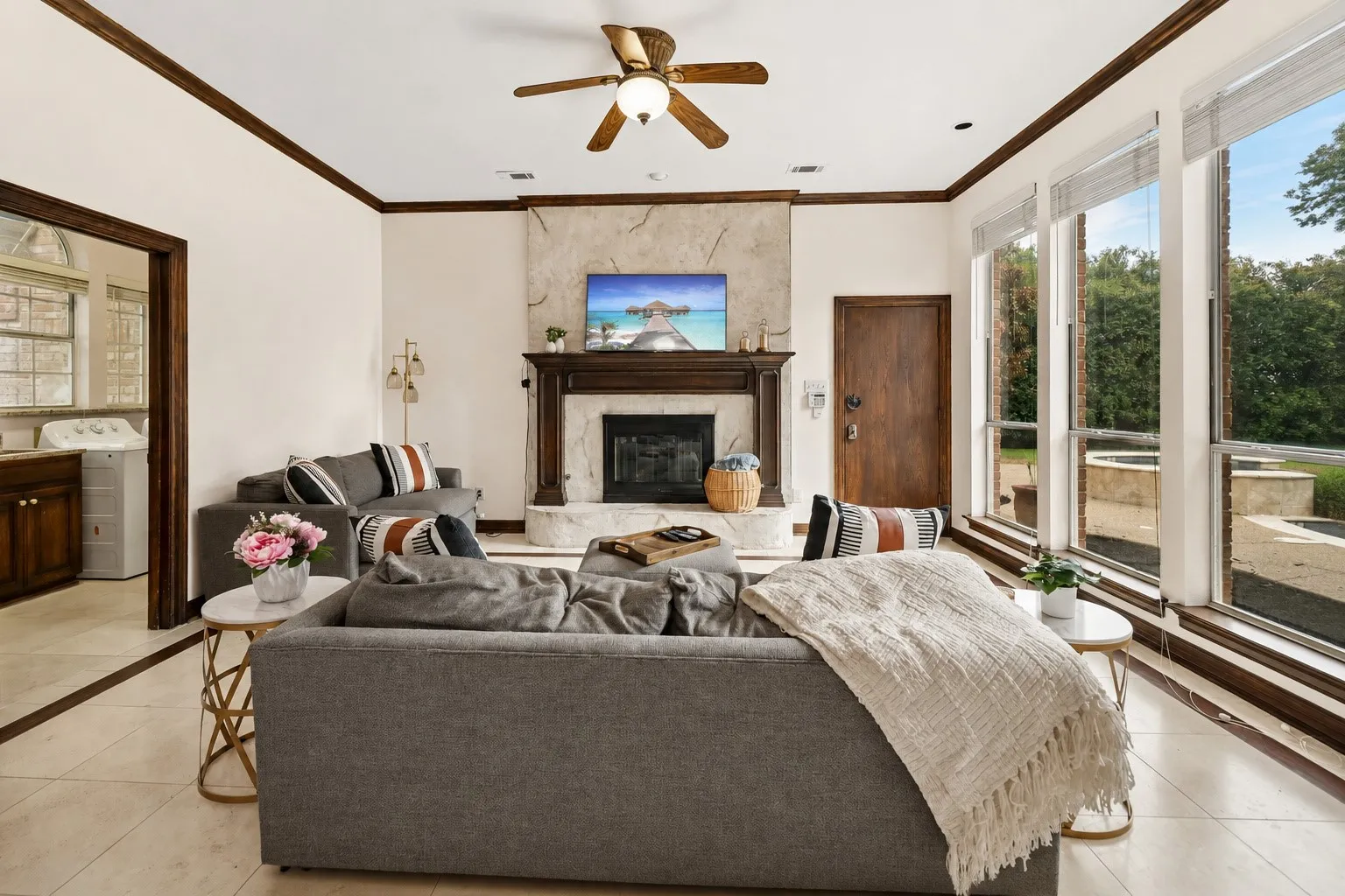 Spacious living area featuring a wood-burning fireplace with a stone surround, a ceiling fan, and large windows