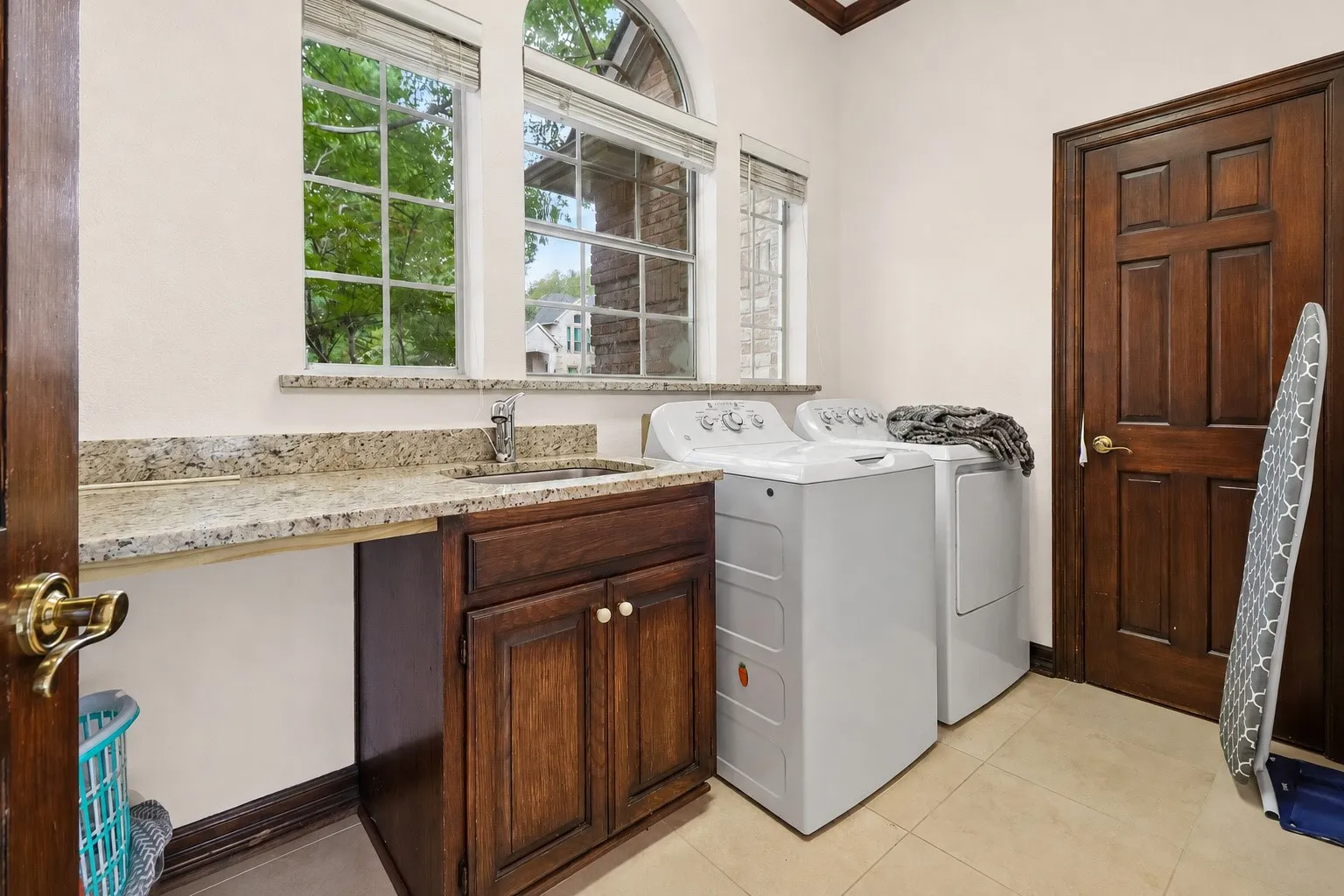 Laundry room featuring a built-in sink, granite countertop, wood cabinetry, and a window with an arched transom