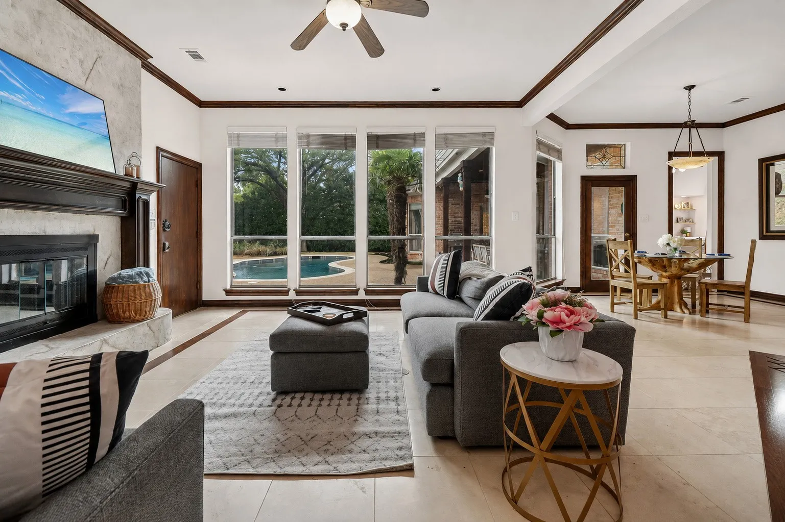 Stone-faced fireplace with a dark wood mantel, large windows overlooking a pool, ceiling fan, recessed lighting, and tile flooring