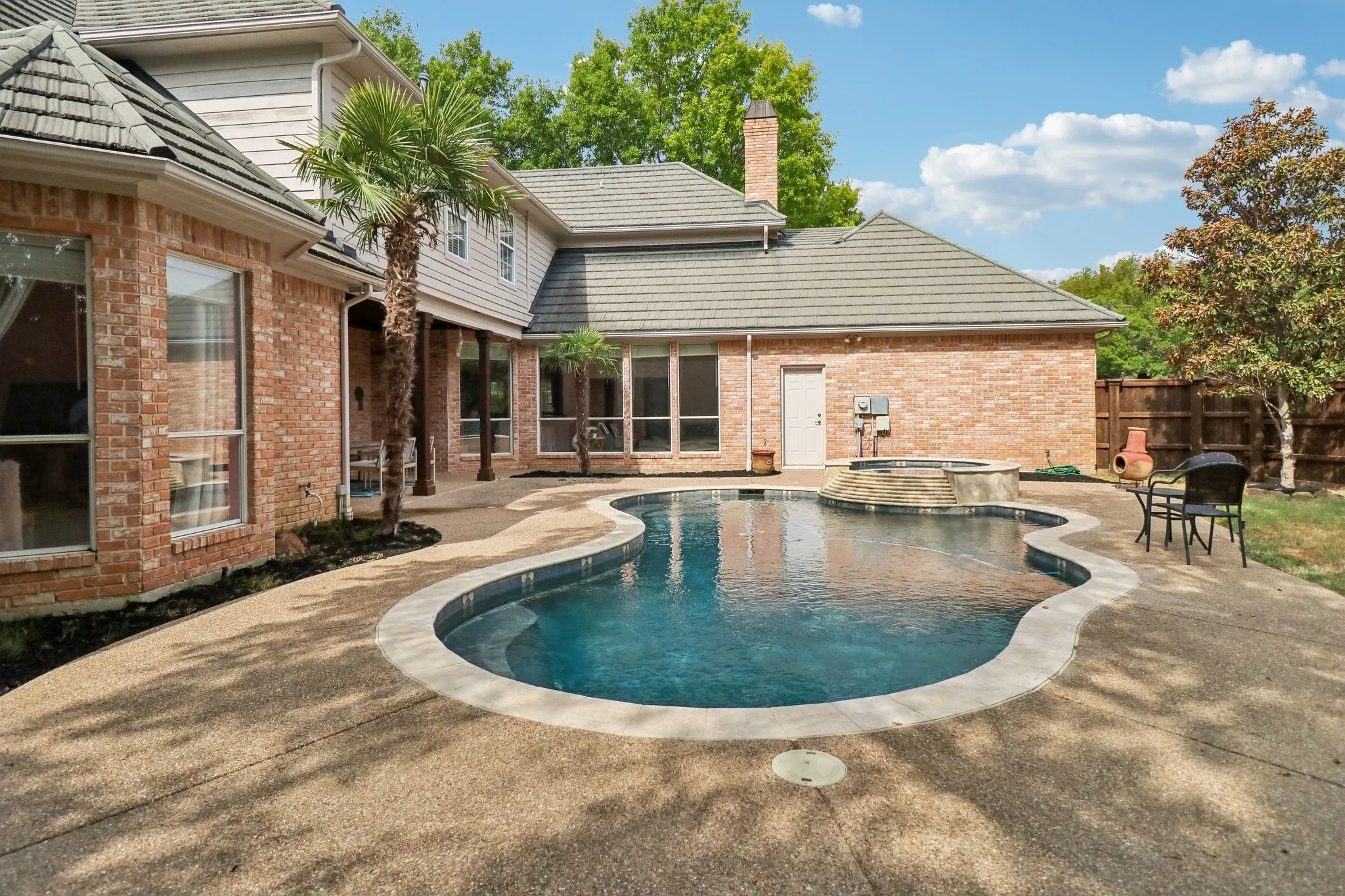 Brick exterior, tile roof, freeform swimming pool, integrated spa, and exposed aggregate patio
