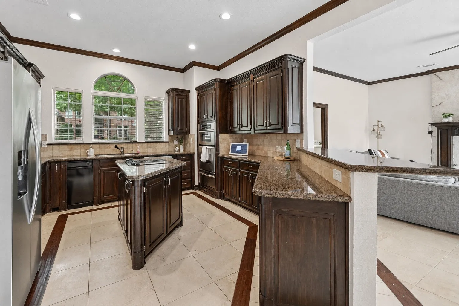 Kitchen featuring dark wood cabinetry, a central island with a stone countertop, built-in stainless steel appliances, and tile flooring with wood-finish inlay