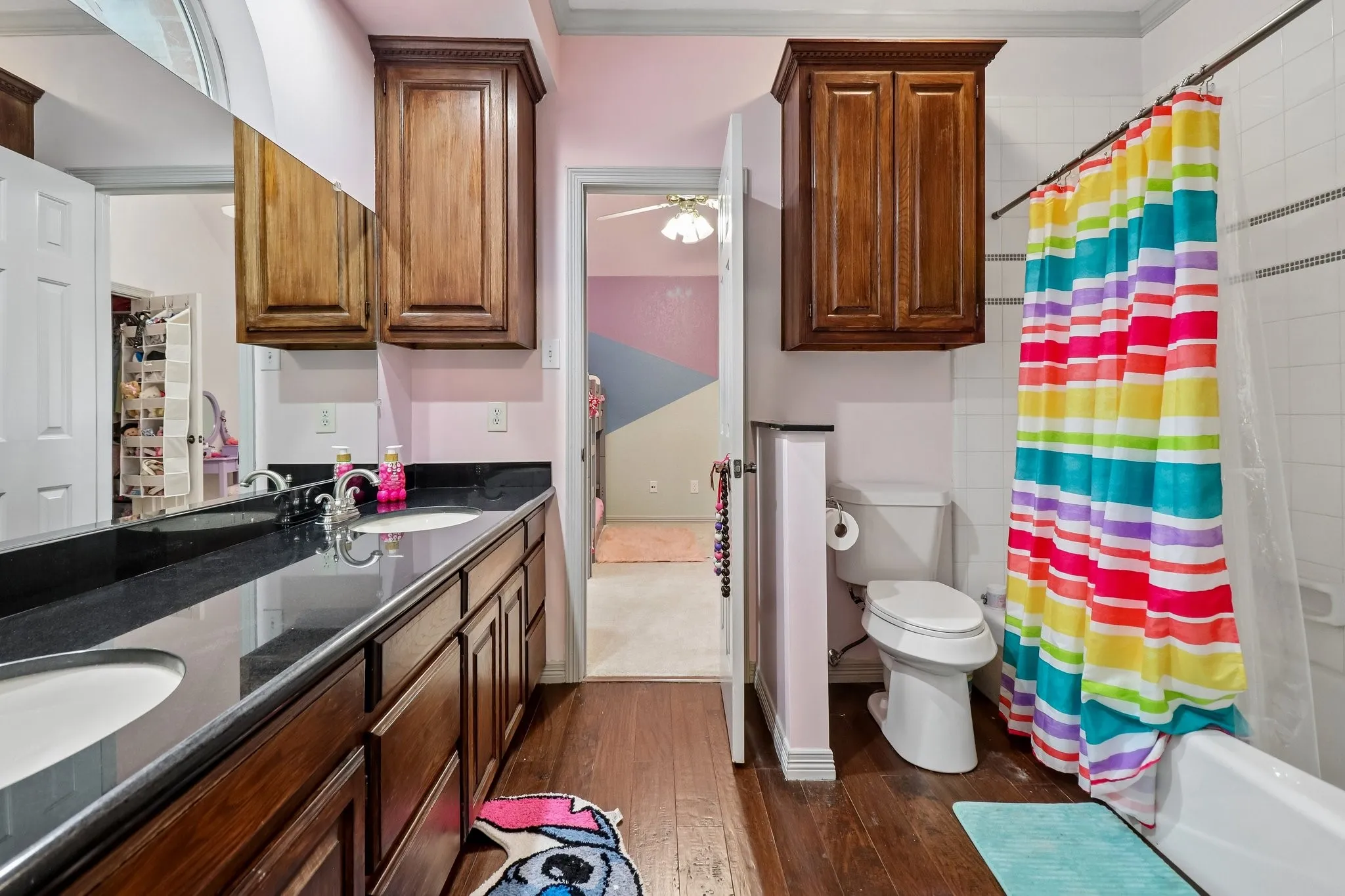 Dual vanity with undermount sinks, black countertop, wood-finish cabinetry, and wood-finish flooring