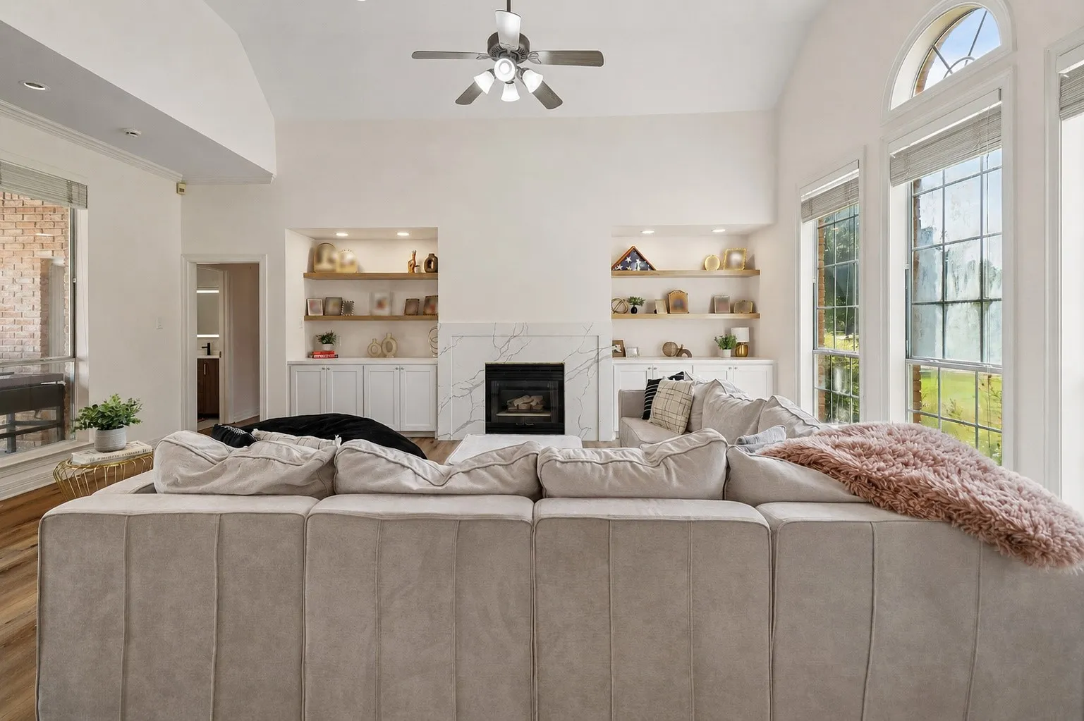 Vaulted ceilings, a built-in fireplace with a white stone surround, integrated shelving, built-in cabinetry, and large windows with arched transoms