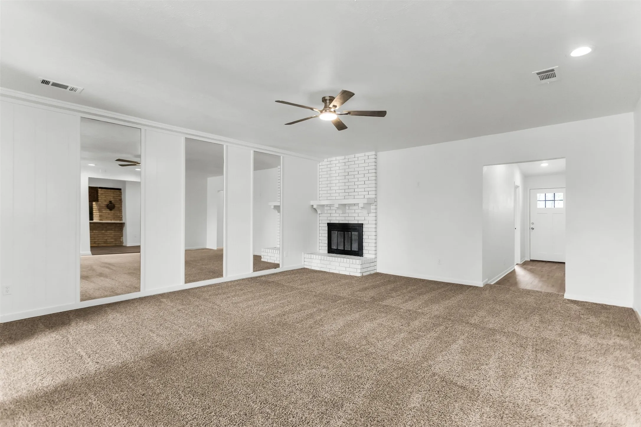 Living area featuring a white brick fireplace, ceiling fan, and mirrored wall panels