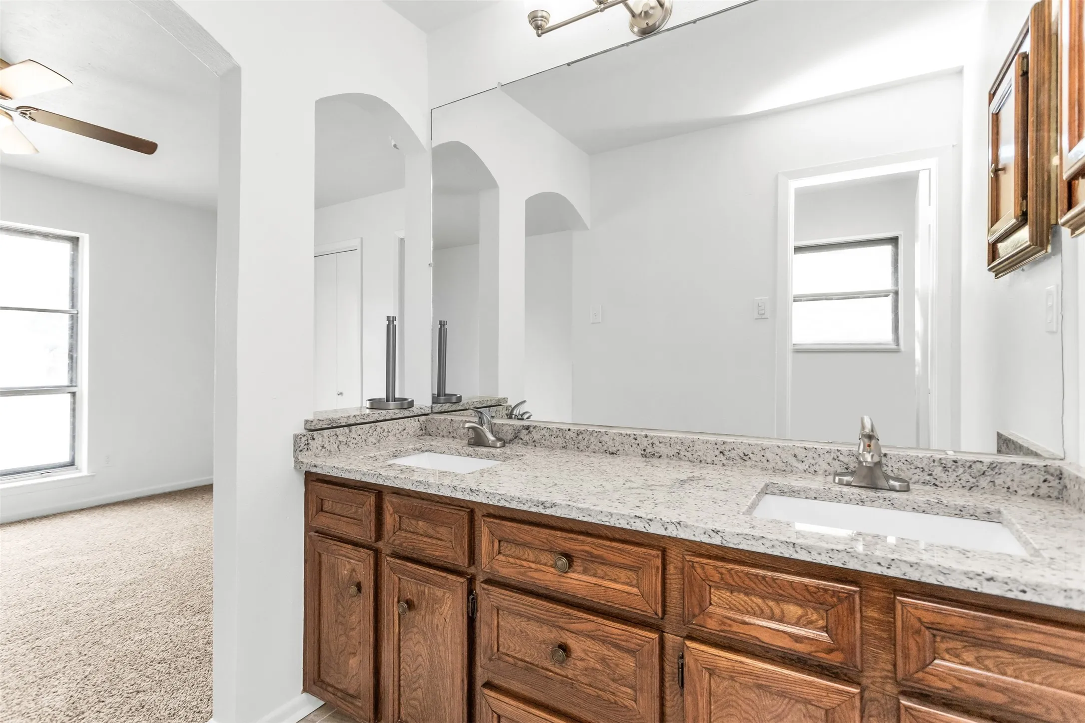 Double vanity with stone countertop, integrated sinks, wood-finish cabinetry, and overhead lighting