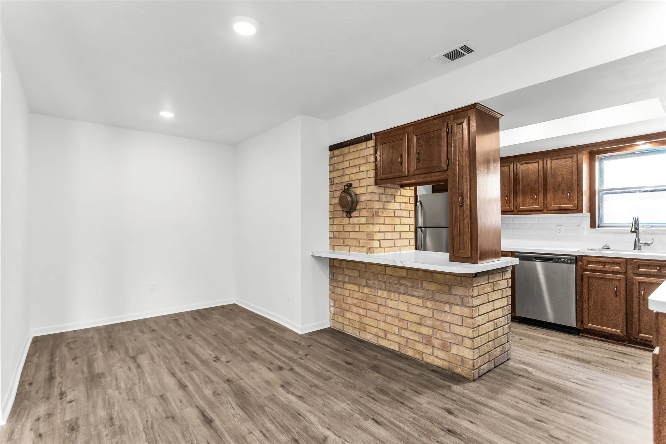 Open-concept living space featuring wood-finish flooring, recessed lighting, a brick breakfast bar, and dark wood cabinetry