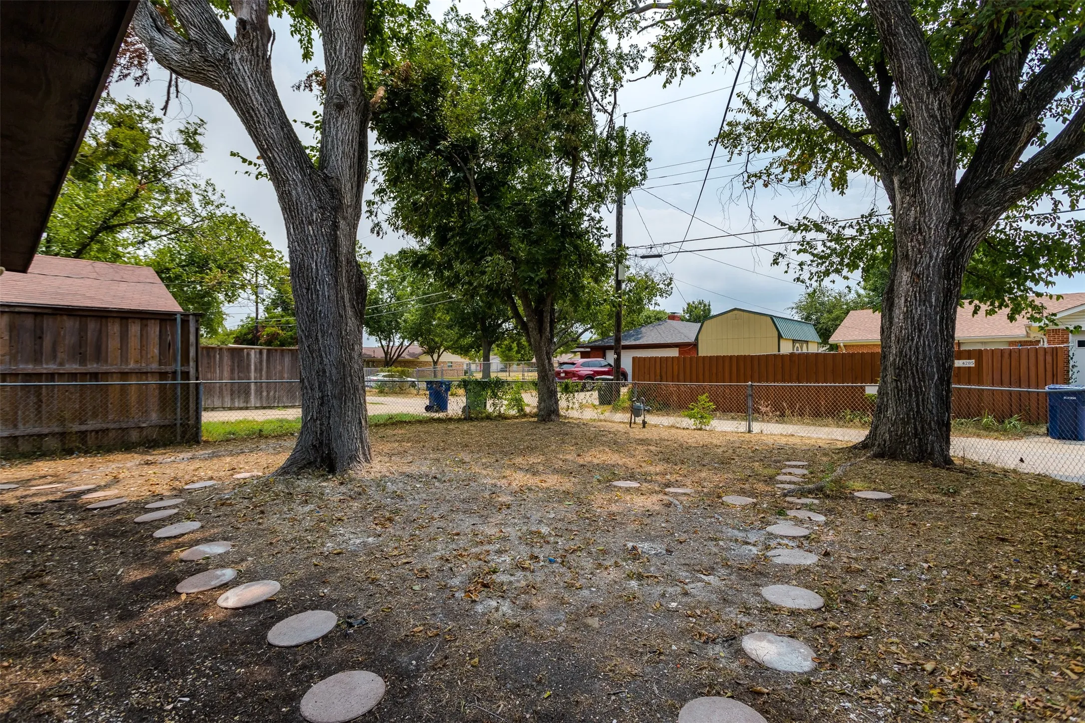 Expansive yard with mature trees, a storage shed, wood fencing, and a chain-link fence