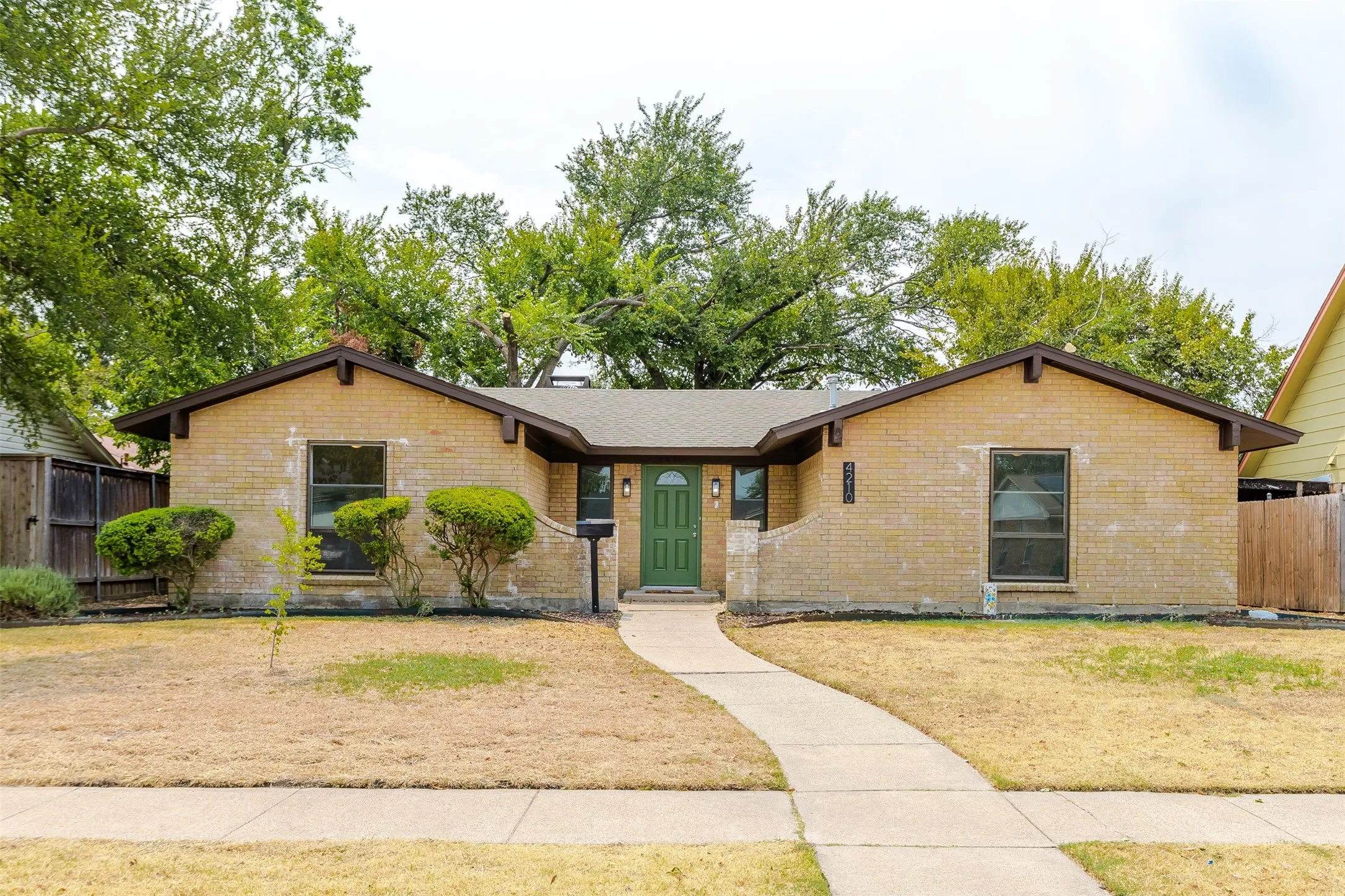 Brick facade, gabled roofline, green front door, concrete pathway, and mature trees