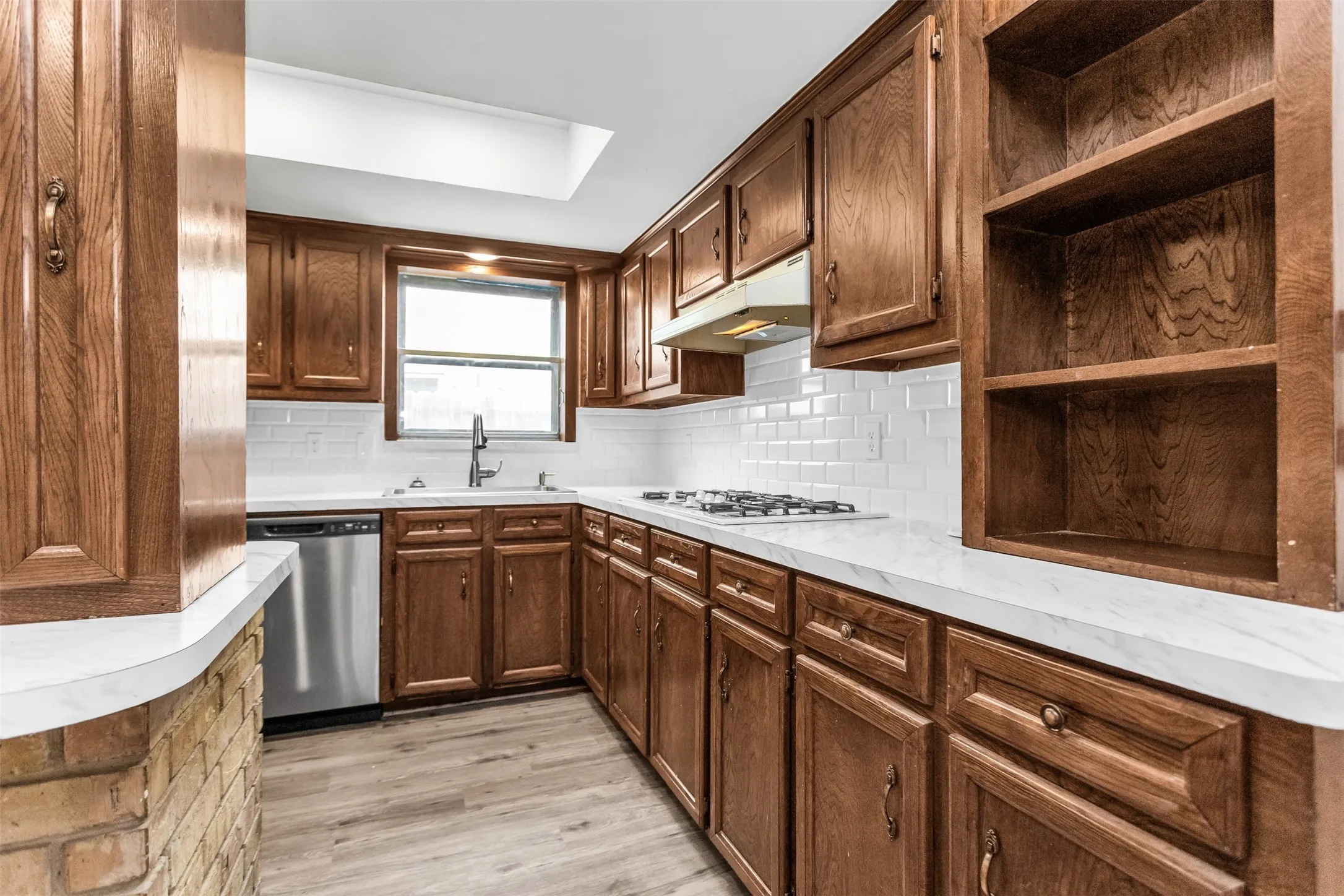 Wood cabinetry with integrated open shelving, white subway tile backsplash, white countertops, stainless steel appliances, and wood-finish flooring