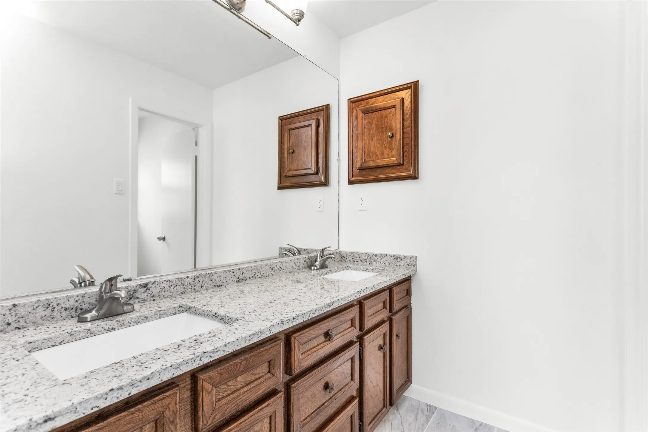 Double vanity with granite countertop, integrated rectangular sinks, and wood-finish cabinetry