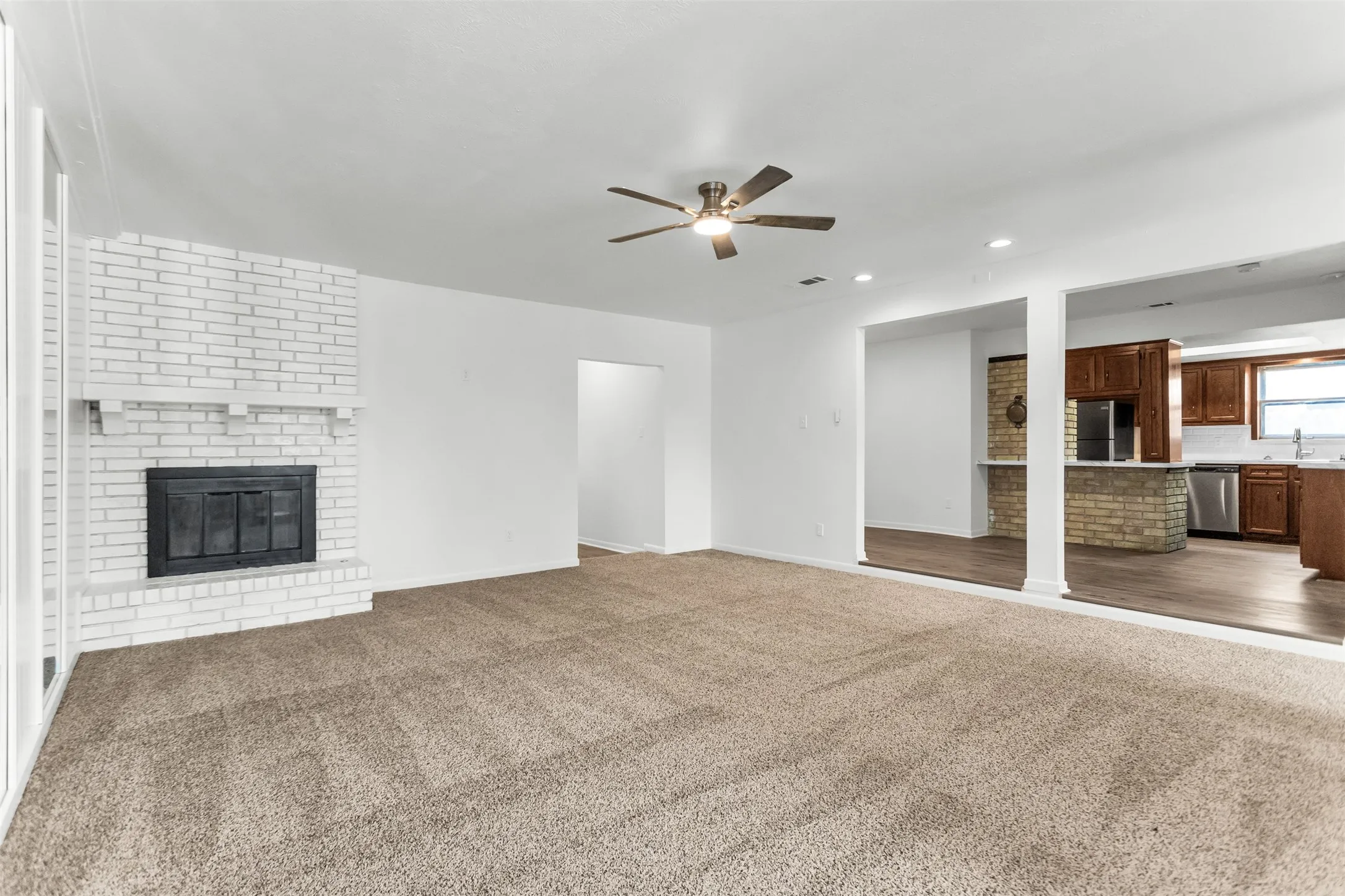 Spacious living area featuring a white brick fireplace with mantel, ceiling fan, and carpeted flooring