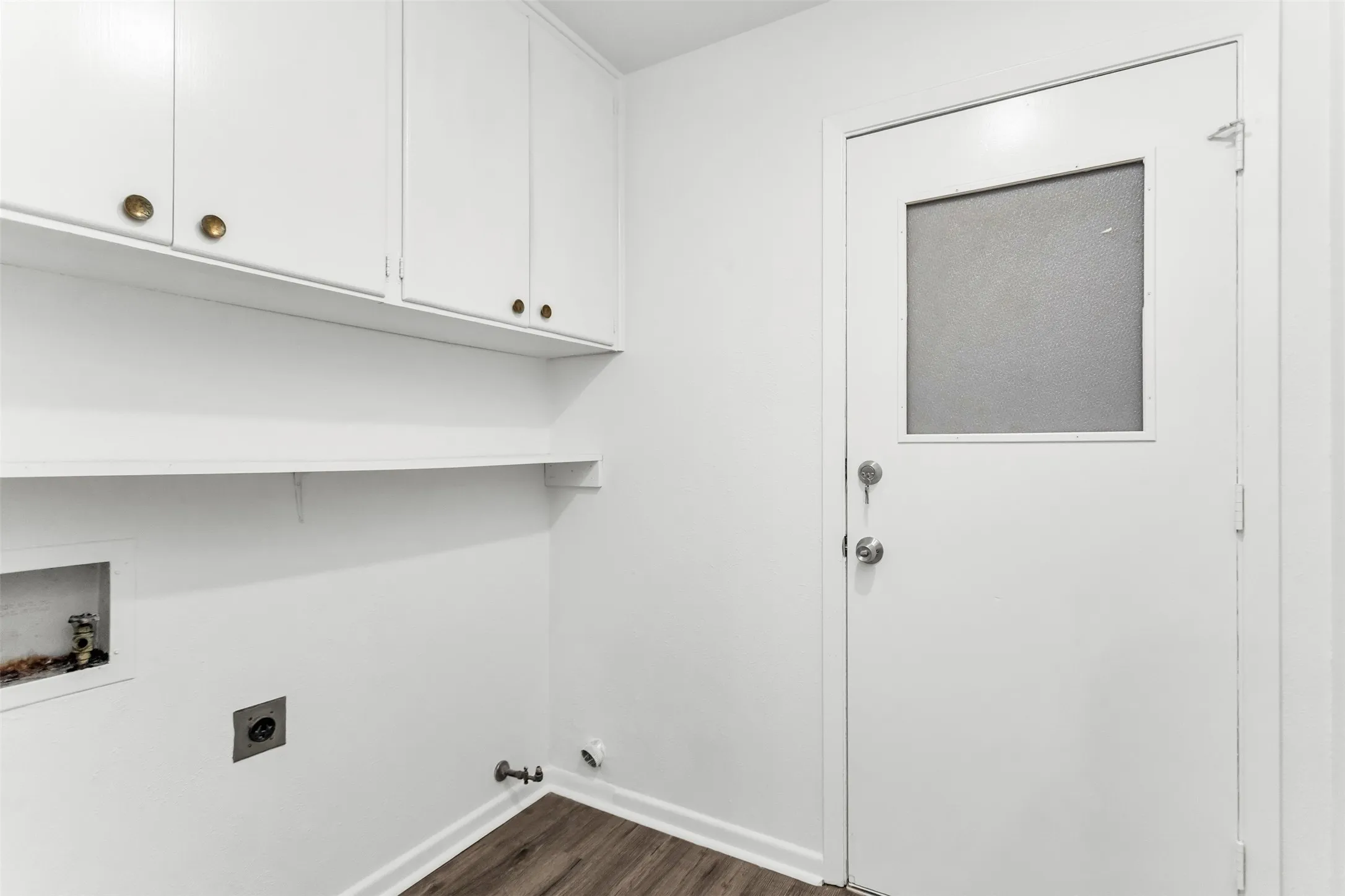 White cabinetry with brass-finish hardware, built-in shelving, wood-finish flooring, and a door with an inset privacy glass panel