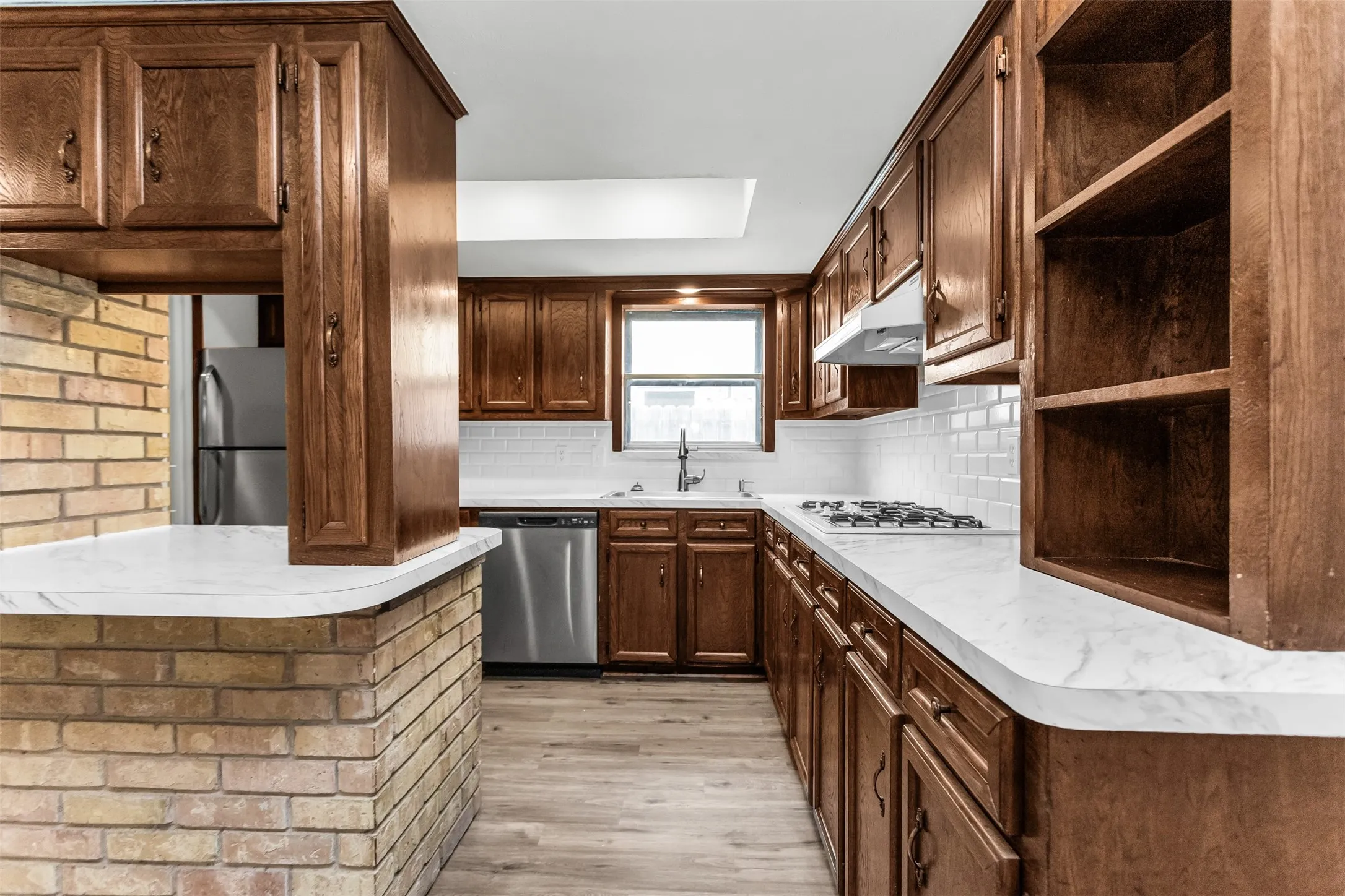 Kitchen featuring wood cabinetry, white subway tile backsplash, light-toned countertops, and wood-finish flooring