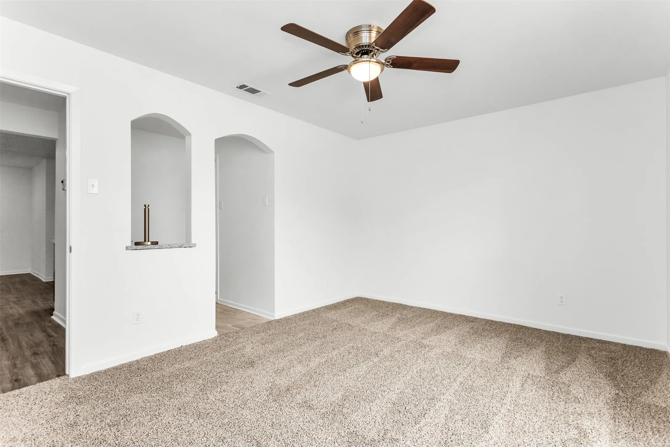 Carpeted living space with a ceiling fan, arched wall niches, and wood-finish flooring in the adjacent area