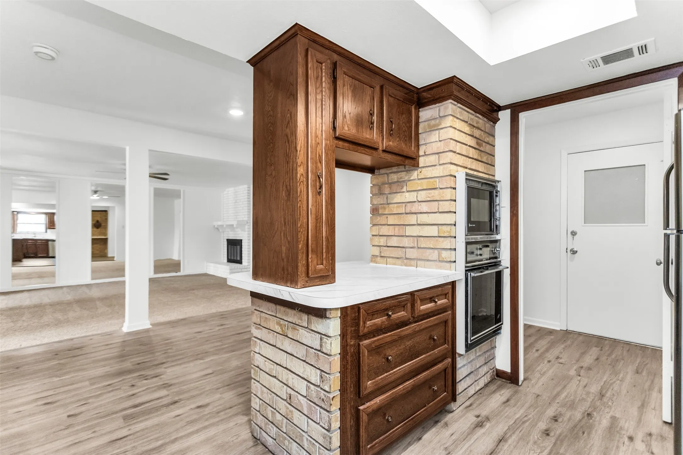 Brick-clad kitchen peninsula with wood cabinetry, integrated wall oven, built-in microwave, and wood-finish flooring