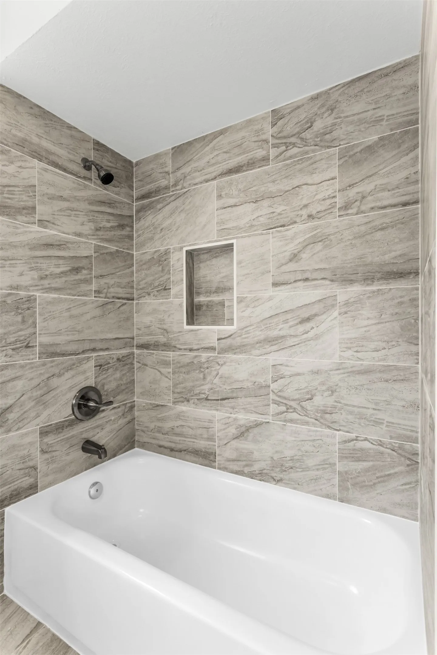 Bathtub with full-height tile surround, integrated shower niche, and dark bronze fixtures