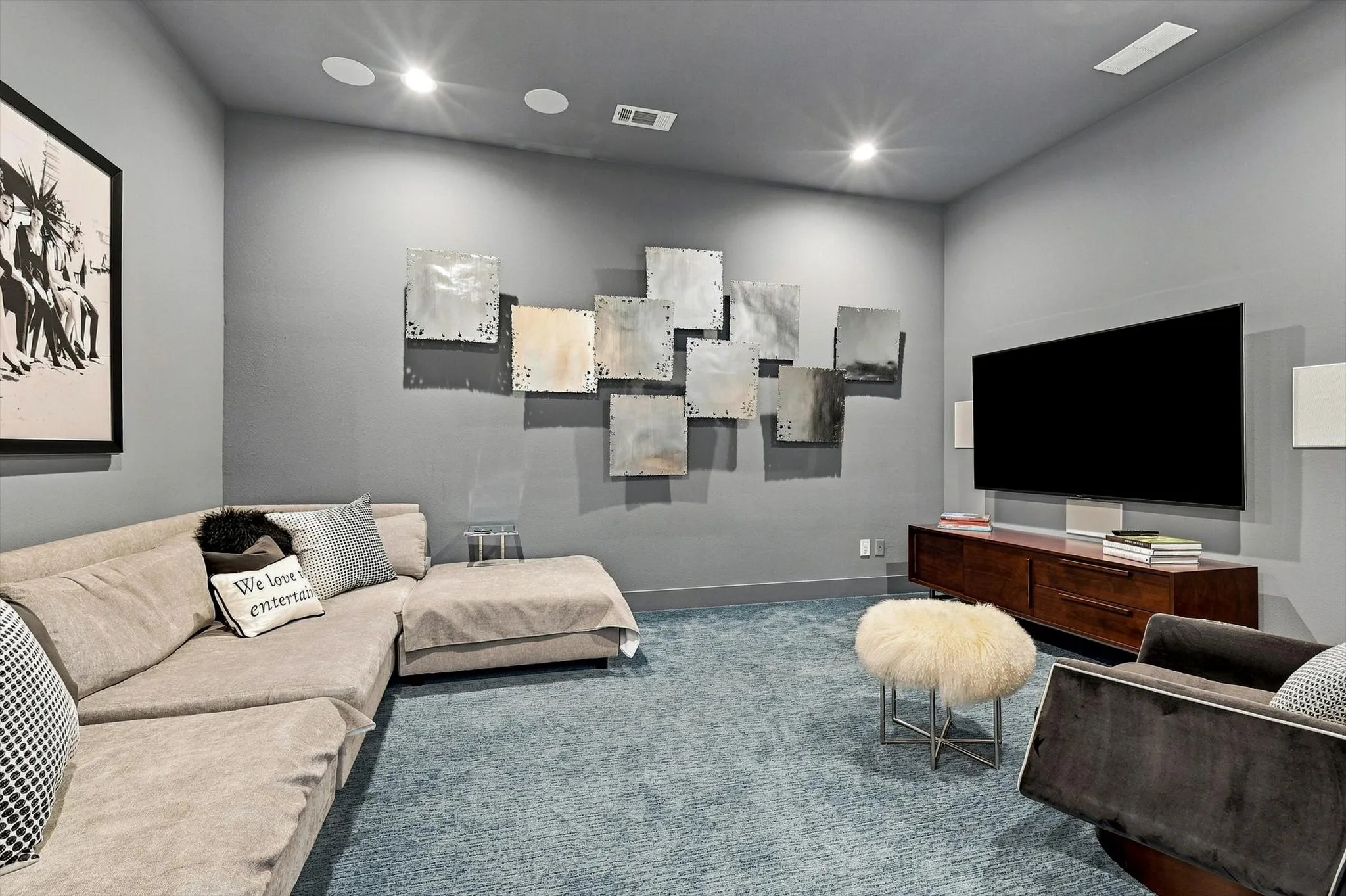 Recessed lighting, integrated ceiling speakers, wall-mounted television, built-in media console with wood finish, and wall-to-wall carpet