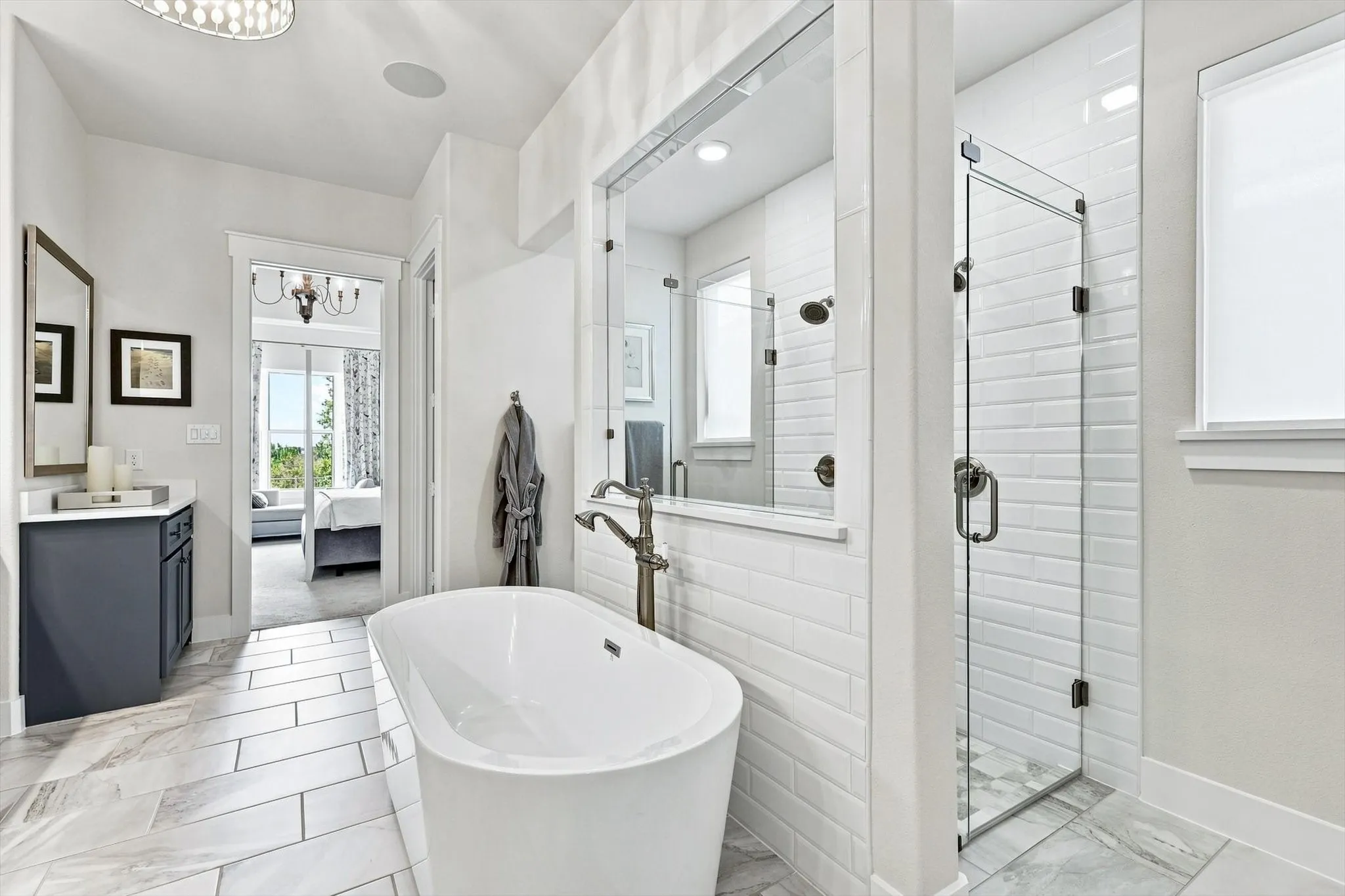 Freestanding soaking tub, frameless glass shower enclosure, wood-finish tile flooring, white subway tile shower surround, and a single vanity with dark cabinetry