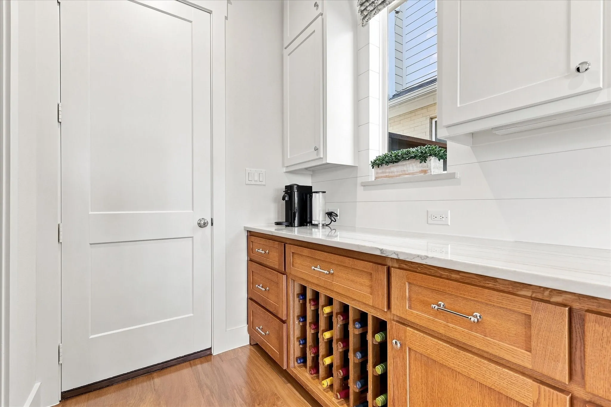 Built-in wood-finish cabinetry featuring a wine rack, white upper cabinets, white countertop, and a window with natural light