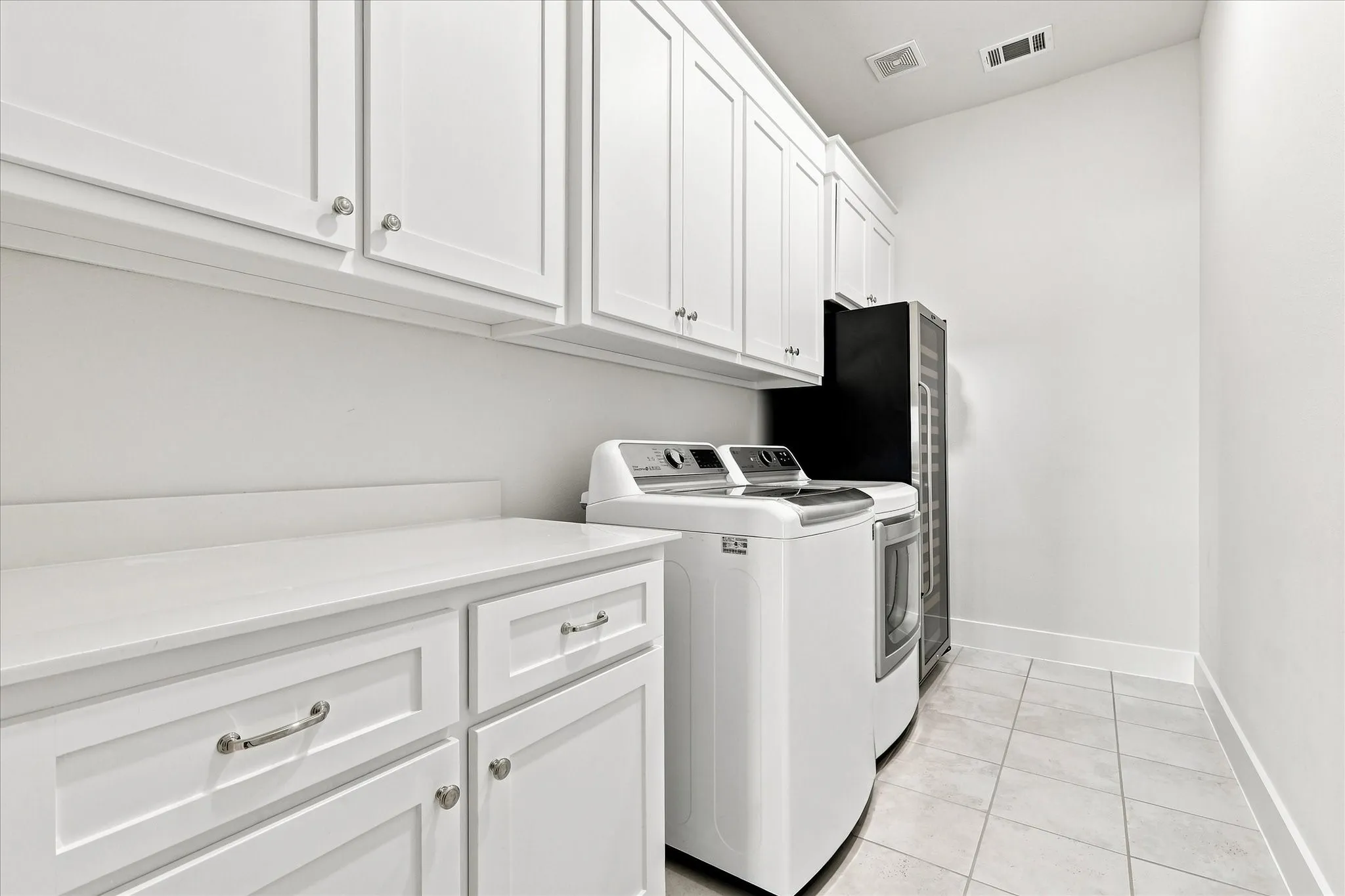 White shaker cabinetry, light-toned countertop, and light tile flooring