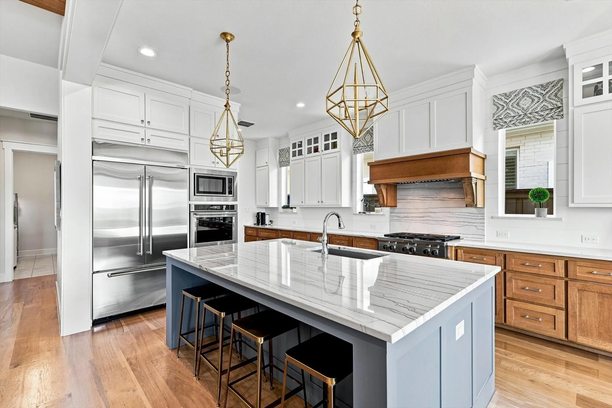 Gourmet kitchen featuring a large central island with seating, stainless steel appliances, white upper cabinetry, and wood-finish lower cabinetry