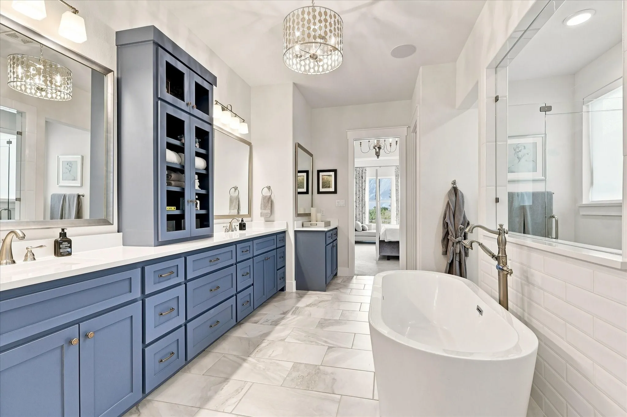 Dual vanity with blue cabinetry and white countertops, freestanding soaking tub with floor-mounted faucet, glass-enclosed shower, and tiled flooring