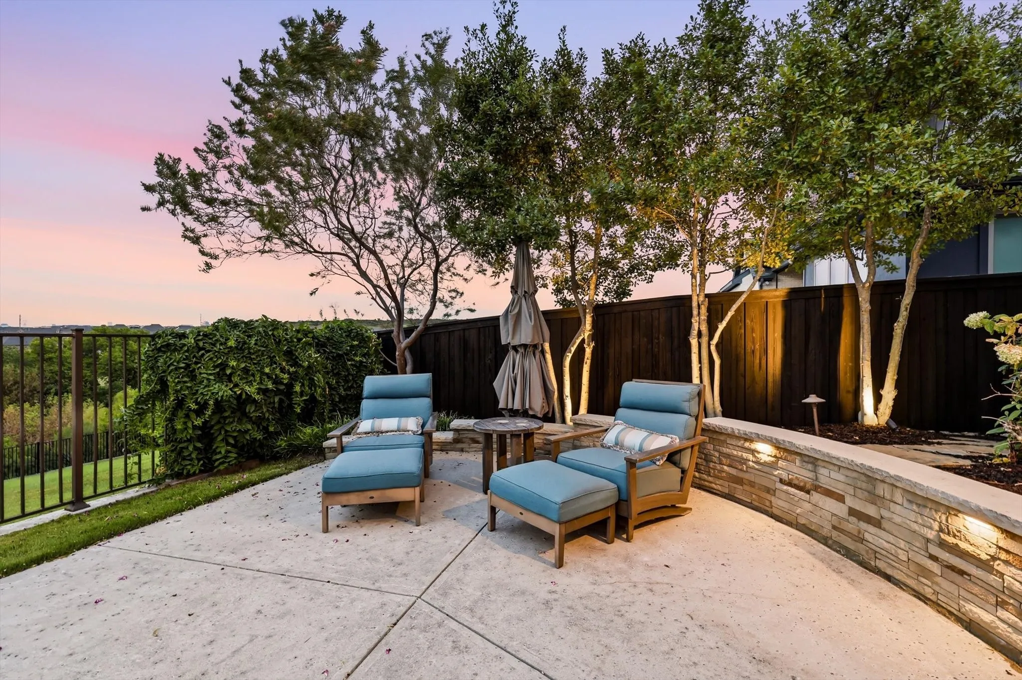 Concrete patio with a stone-clad retaining wall, integrated lighting, and mature trees