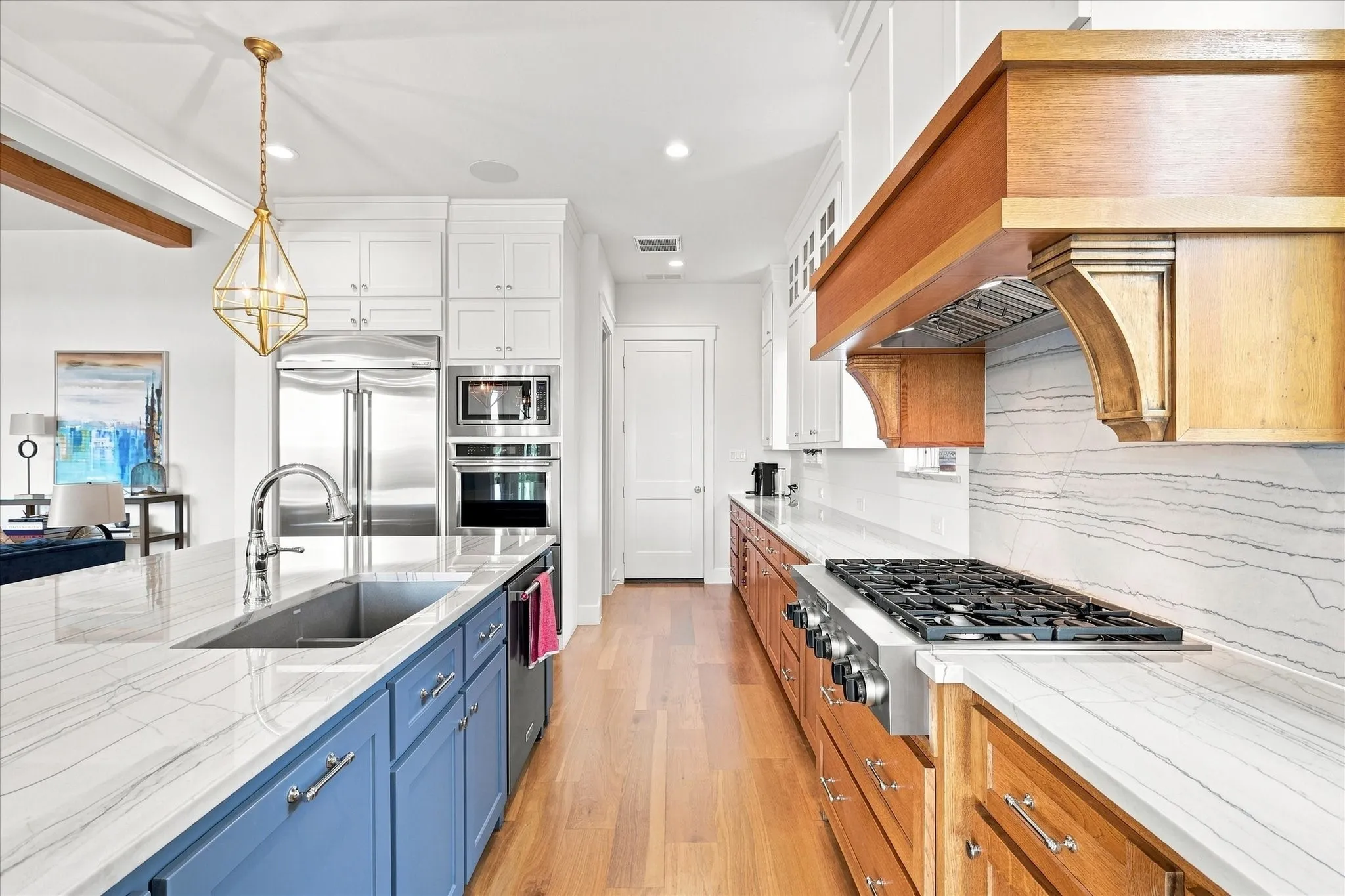 Kitchen featuring stainless steel appliances, wood-finish flooring, white and blue cabinetry, and stone countertops