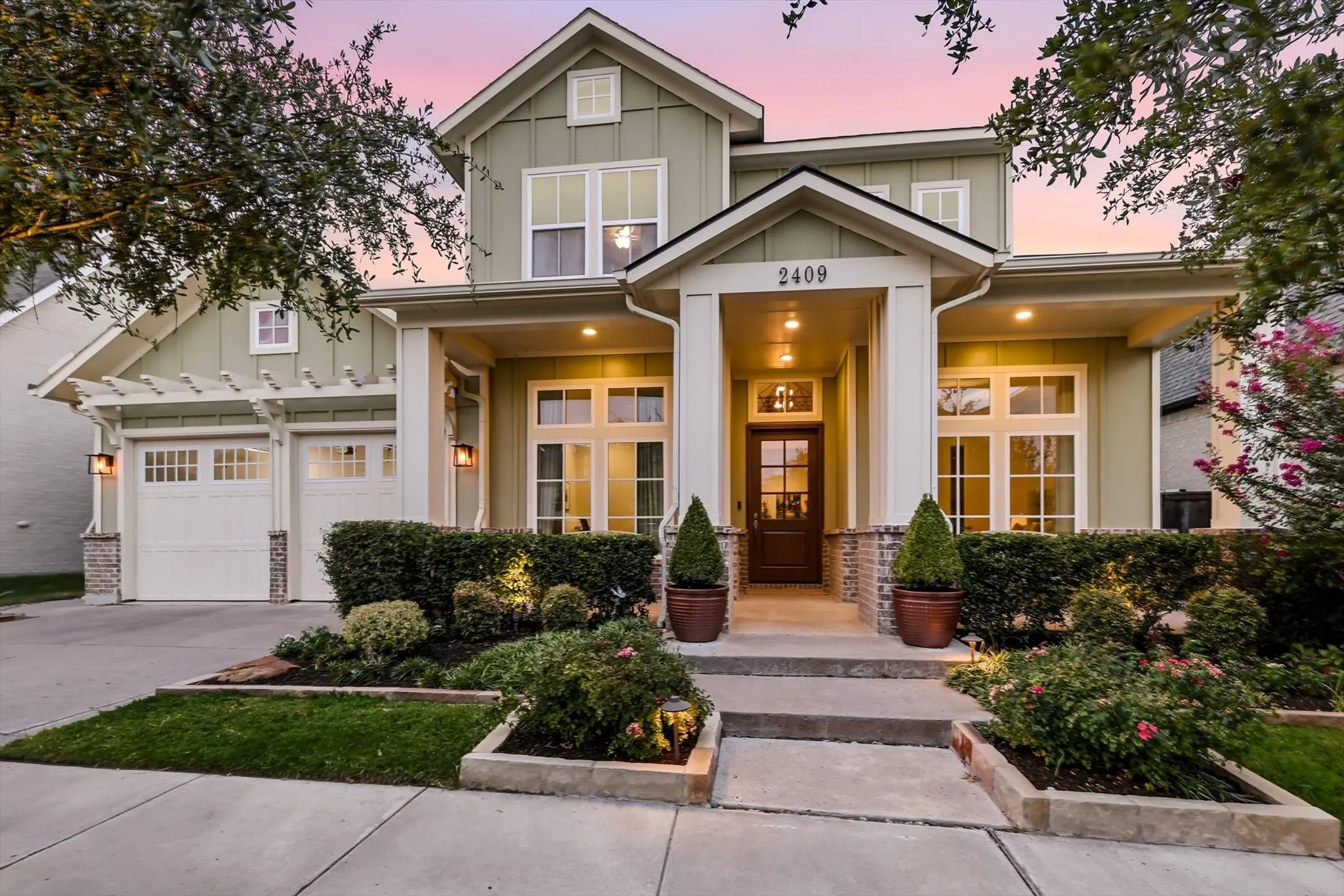 Two-story exterior with board and batten siding, stone facade accents, covered front entry, and attached garage with pergola details