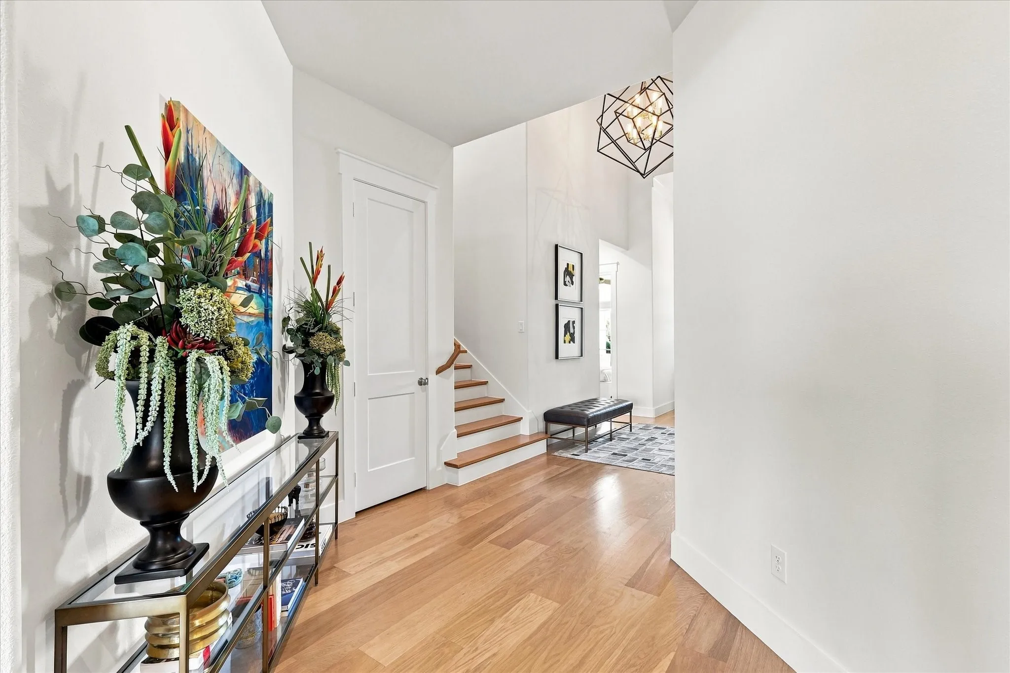 Light wood-finish flooring, white walls, and a geometric chandelier