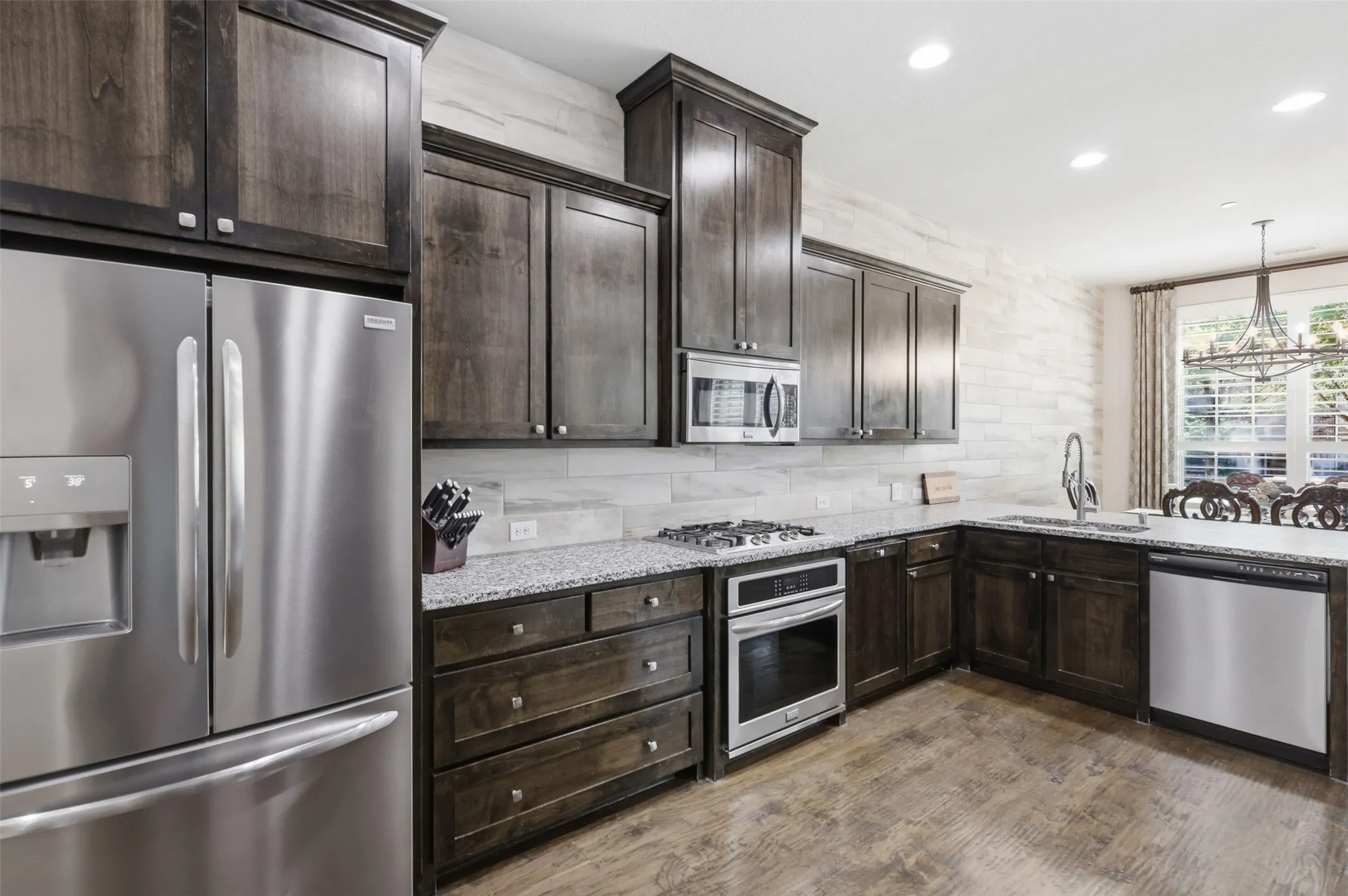 Full kitchen featuring dark wood cabinetry, stainless steel appliances, granite countertops, and wood-finish flooring