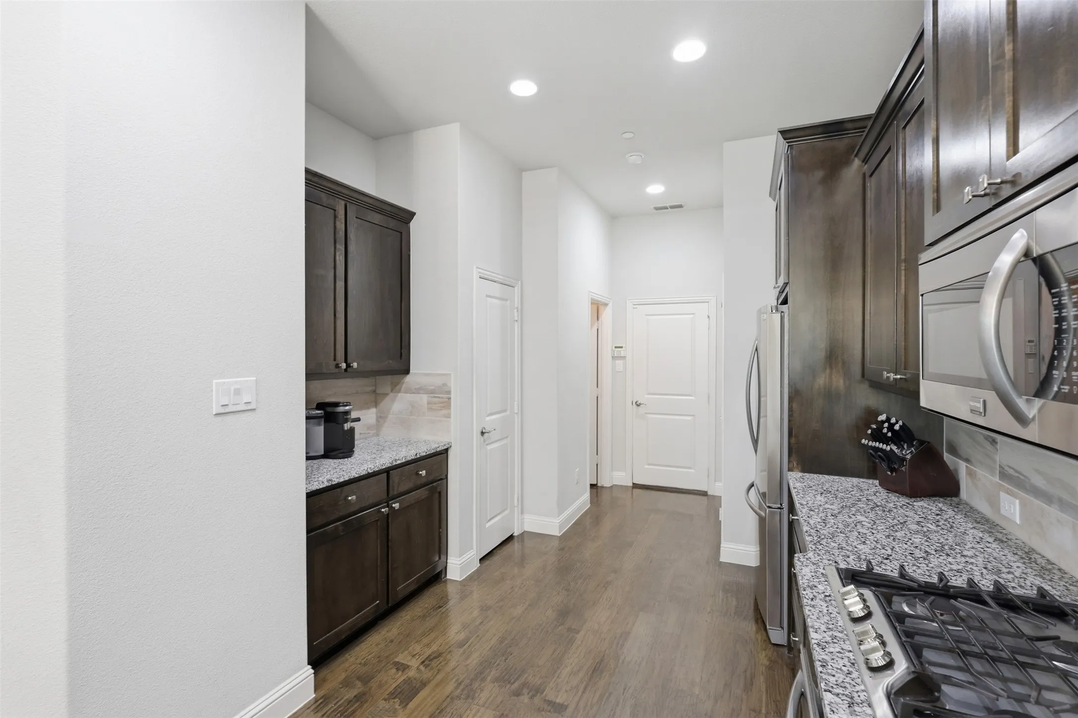 Wood-finish flooring, dark wood cabinetry, granite countertops, stainless steel appliances, and recessed lighting