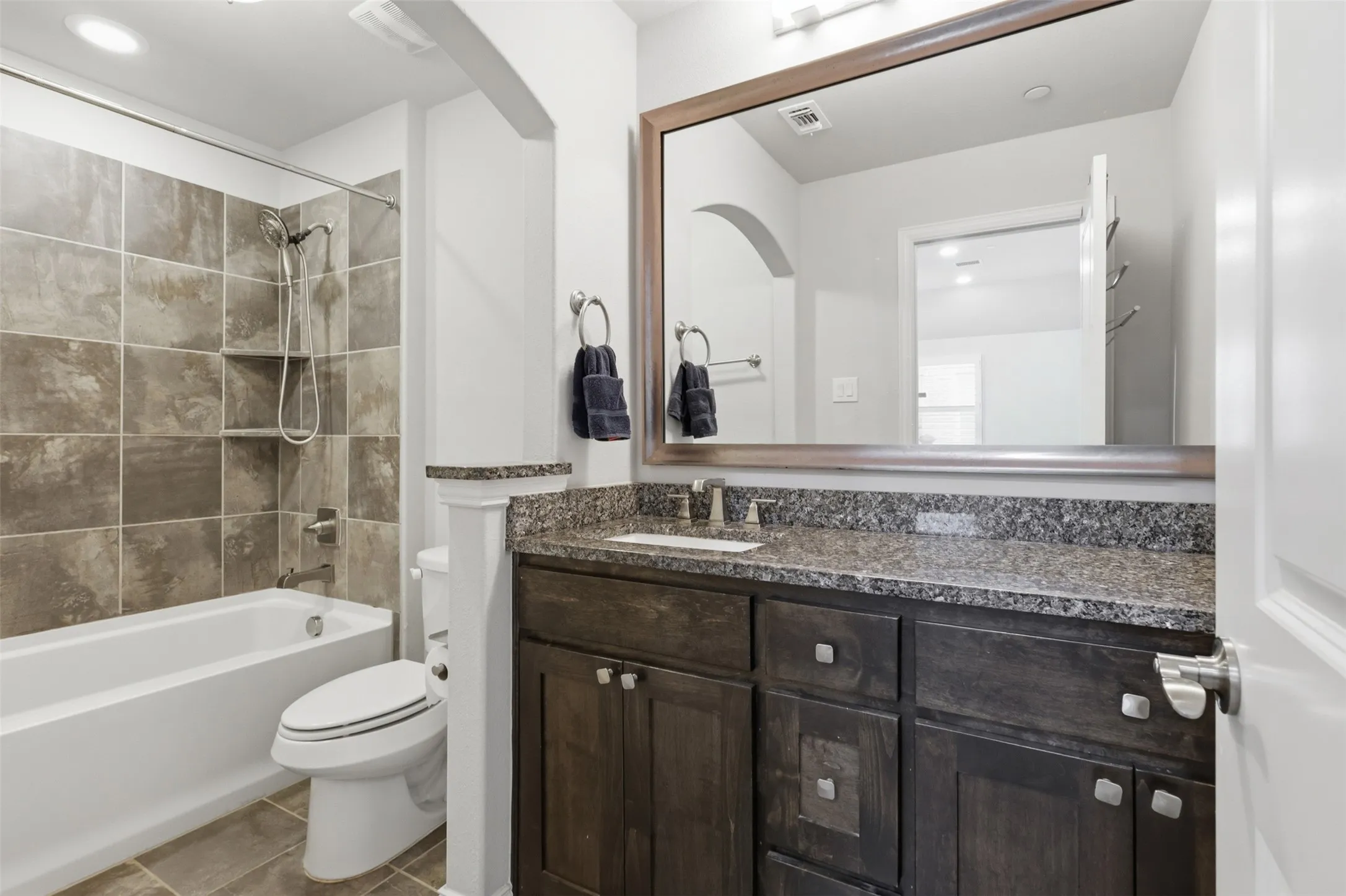 Spacious bathroom featuring a white tub, shower with tile surround and built-in niche, dark wood-finish vanity with granite countertop, and a large framed mirror