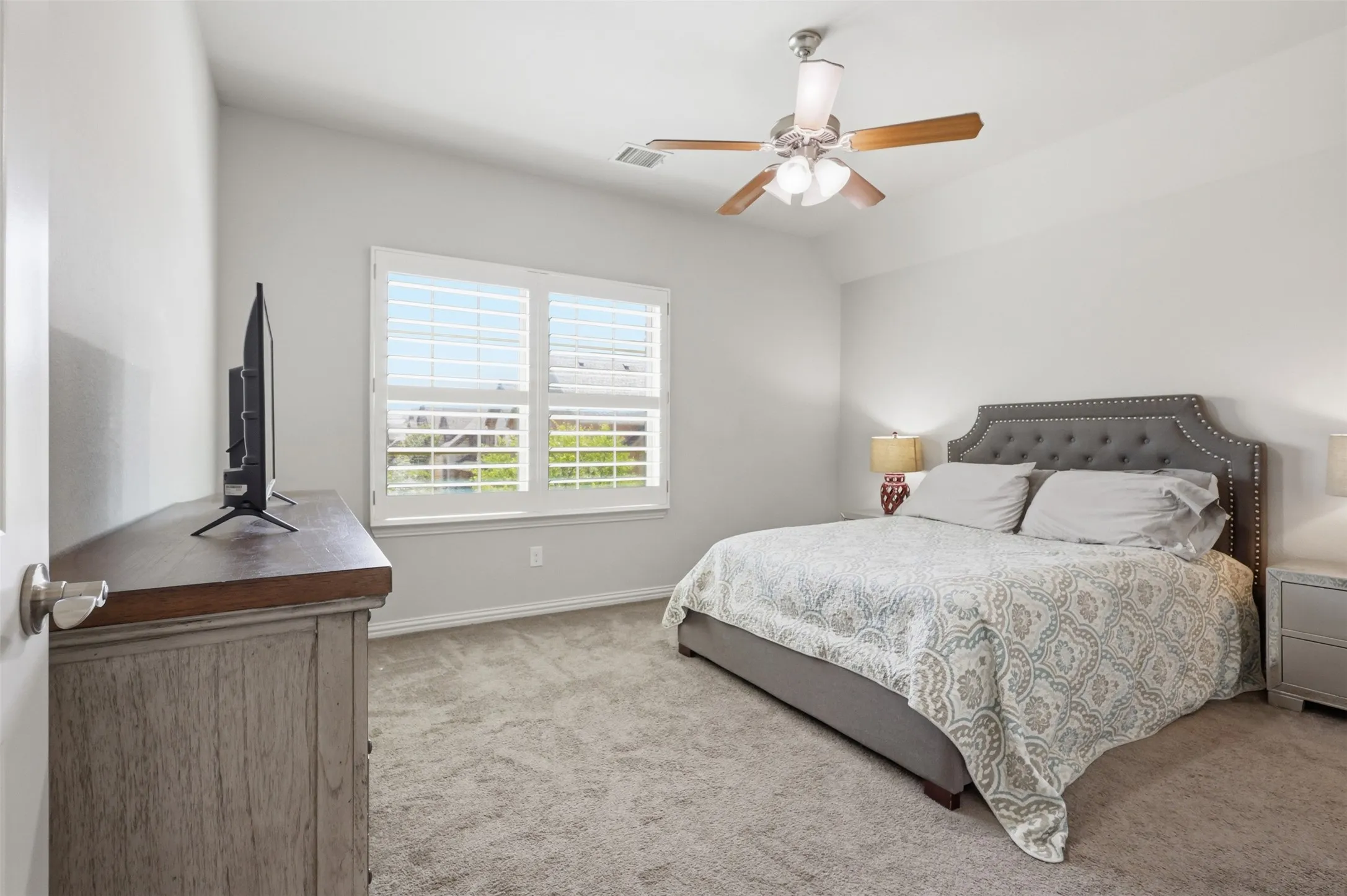 Vaulted ceiling with a ceiling fan, carpeted flooring, and two windows with plantation shutters
