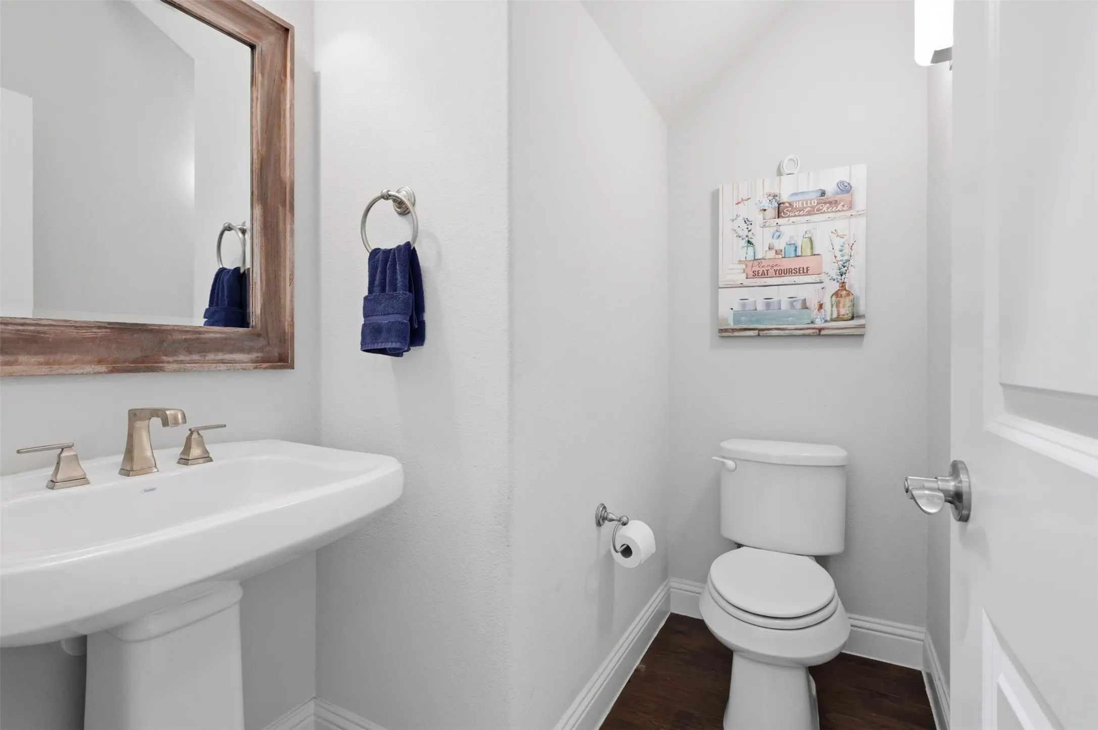 Pedestal sink with brushed nickel faucet, wood-finish flooring, and white baseboards