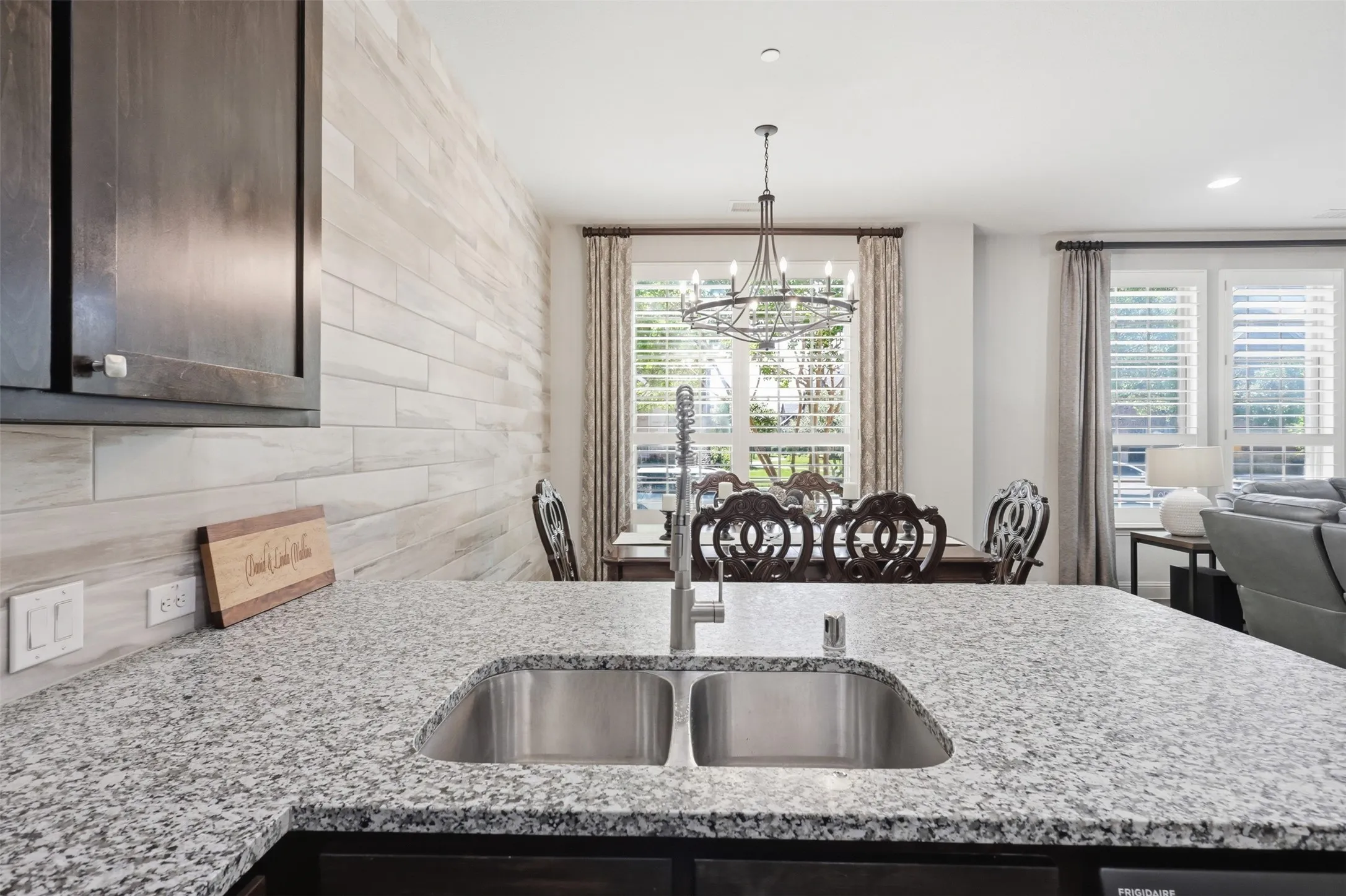 Kitchen island with dual-basin stainless steel sink and granite countertop, dark wood-finish cabinetry, and light wood-plank accent wall