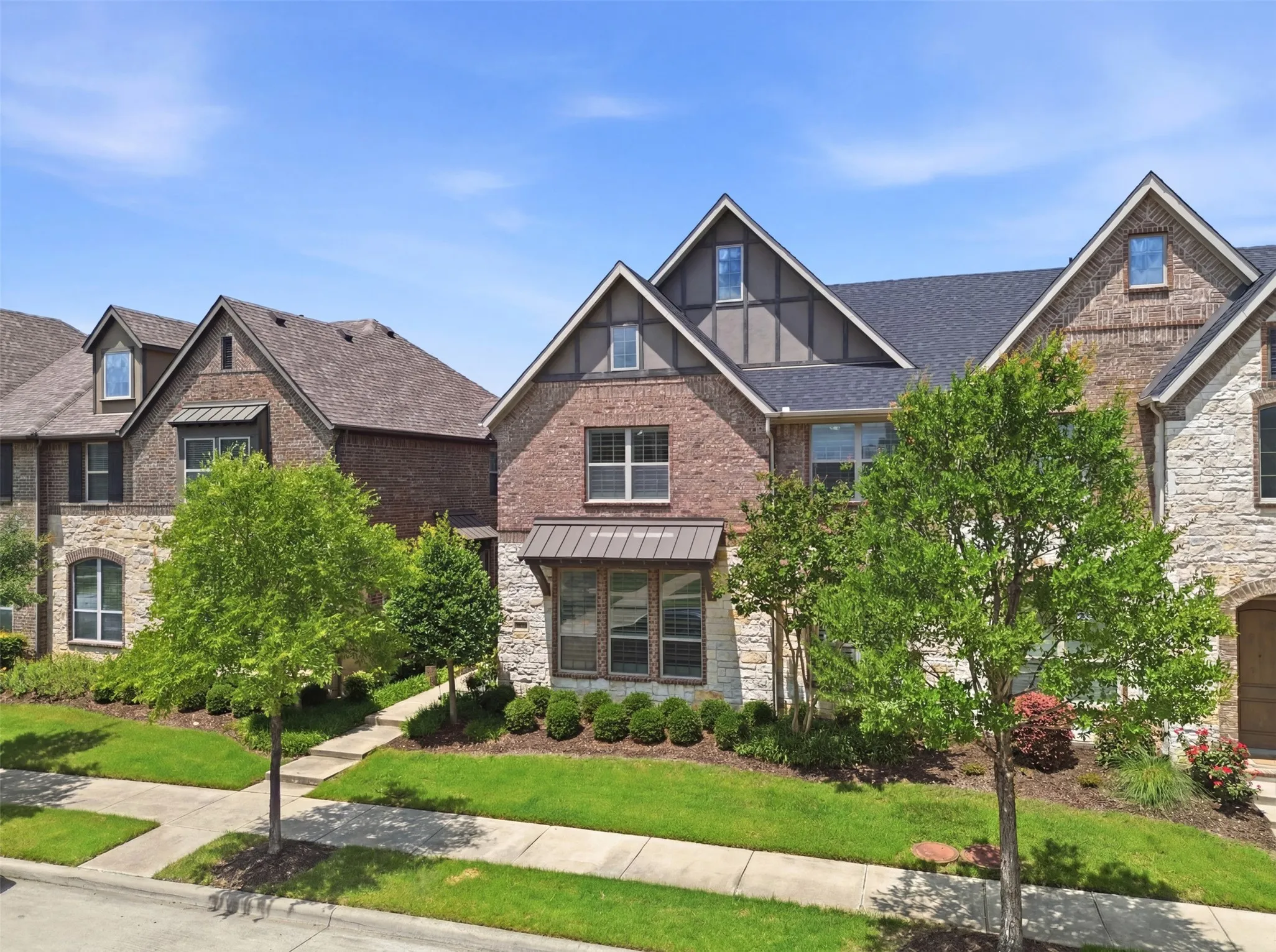 Exterior featuring brick and stone cladding, dark roof shingles, multiple dormer windows, and a metal-accented bay window