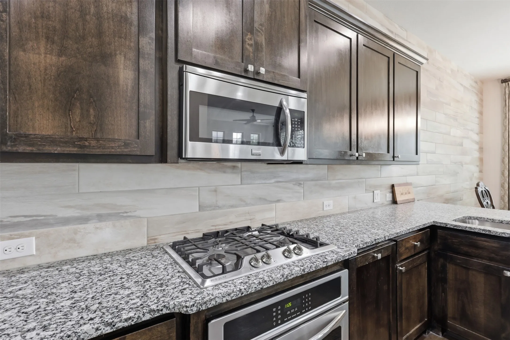 Dark wood cabinetry, speckled countertops, stainless steel microwave, gas cooktop, and built-in oven
