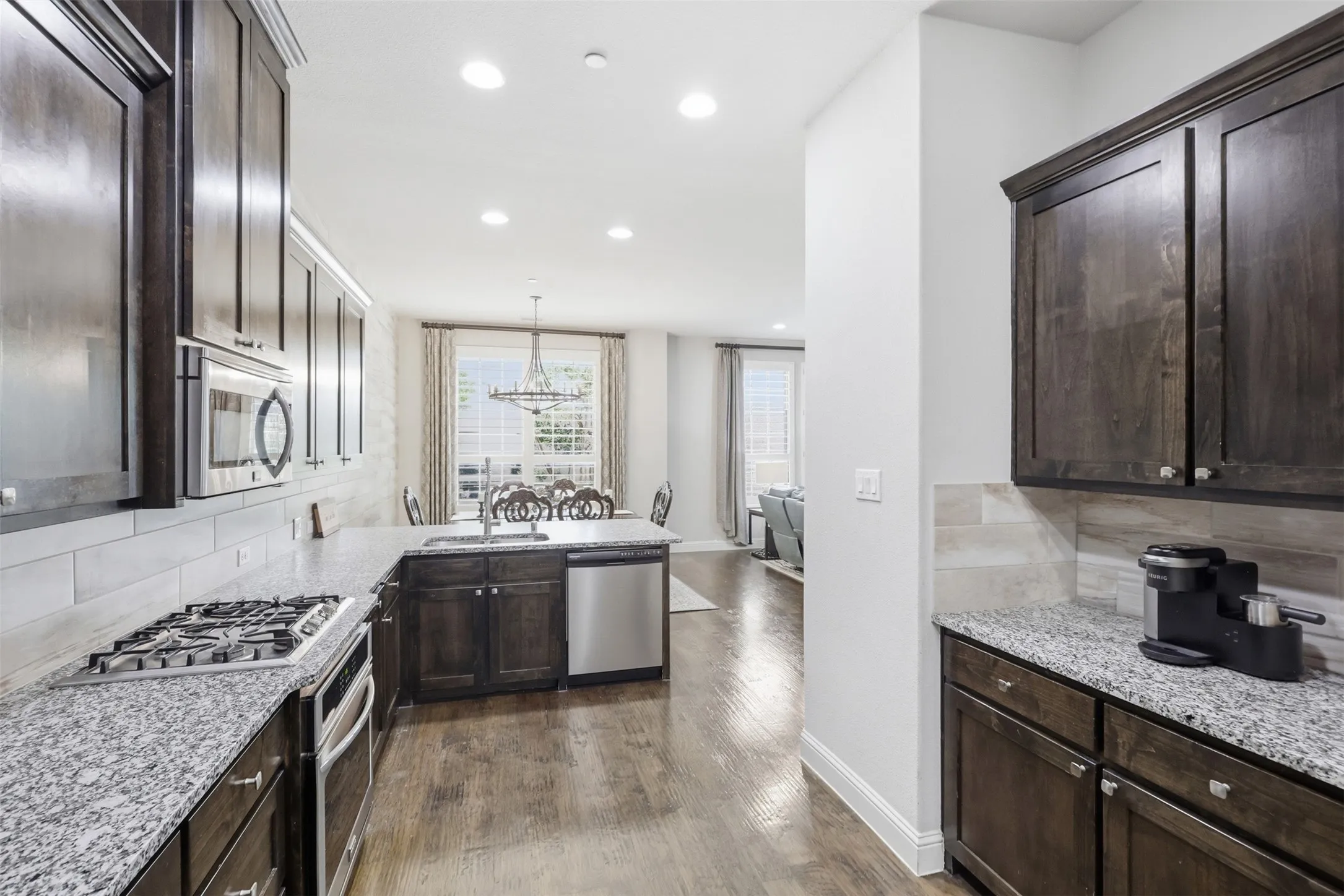 Gourmet kitchen with wood-finish flooring, stainless steel appliances, granite countertops, and dark wood cabinetry