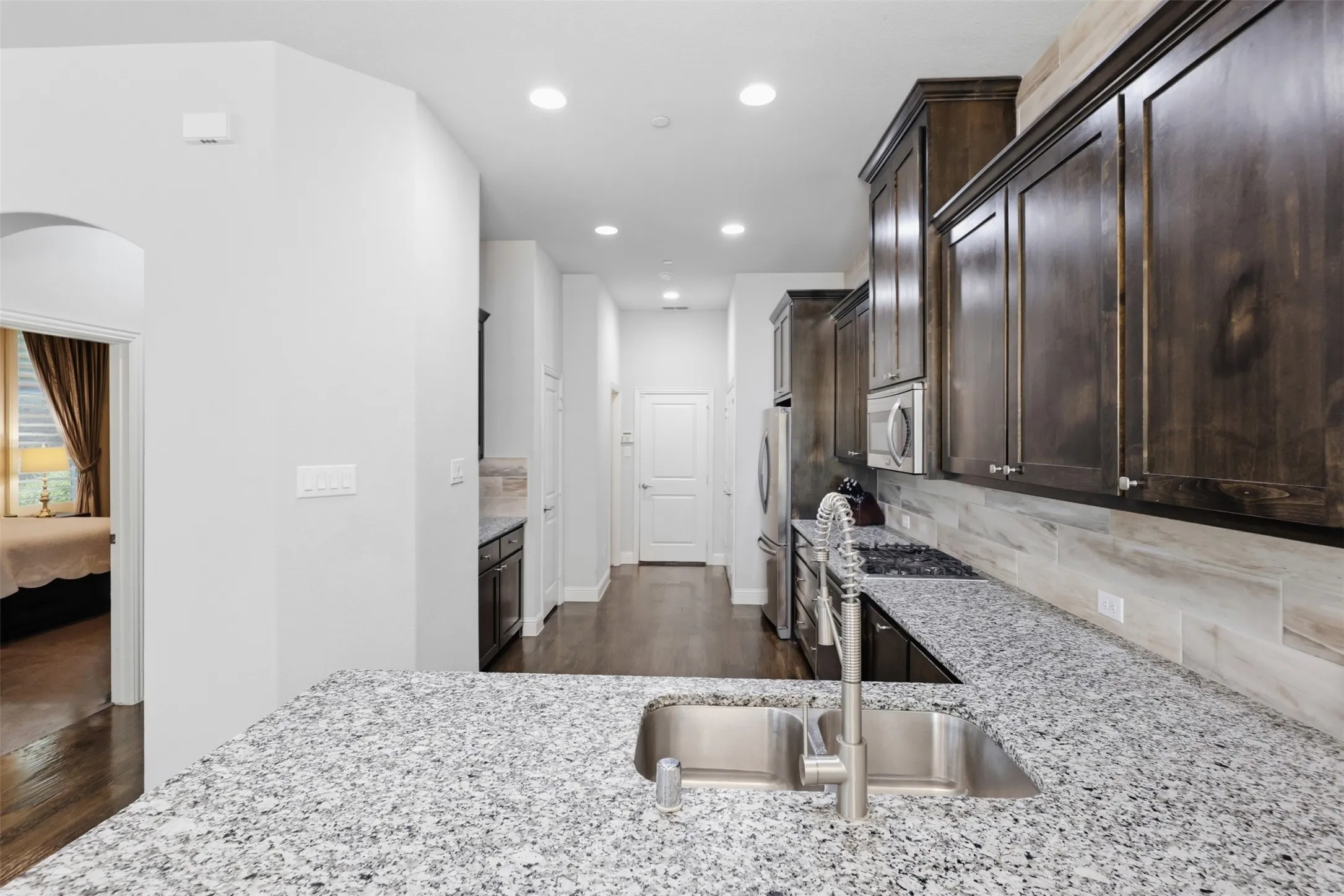 Kitchen featuring an undermount double basin stainless steel sink, granite-finish countertops, wood-finish cabinetry, and a full tile backsplash