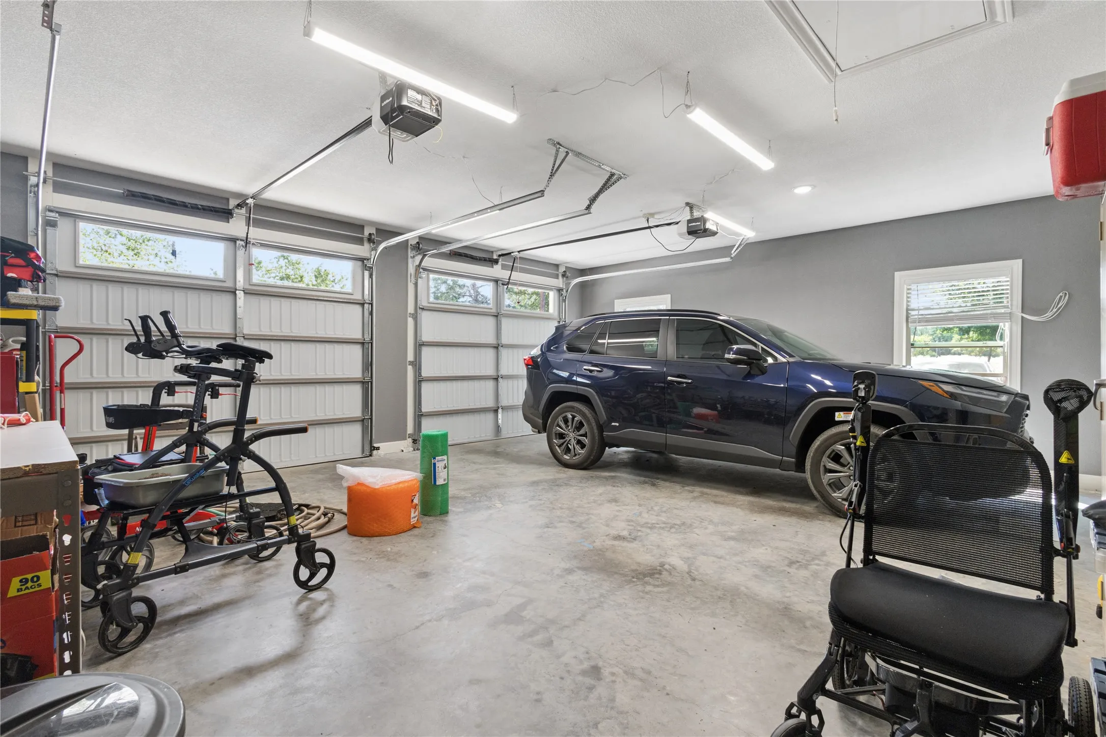 Spacious garage with concrete flooring, two sectional garage doors with upper windows, and overhead strip lighting