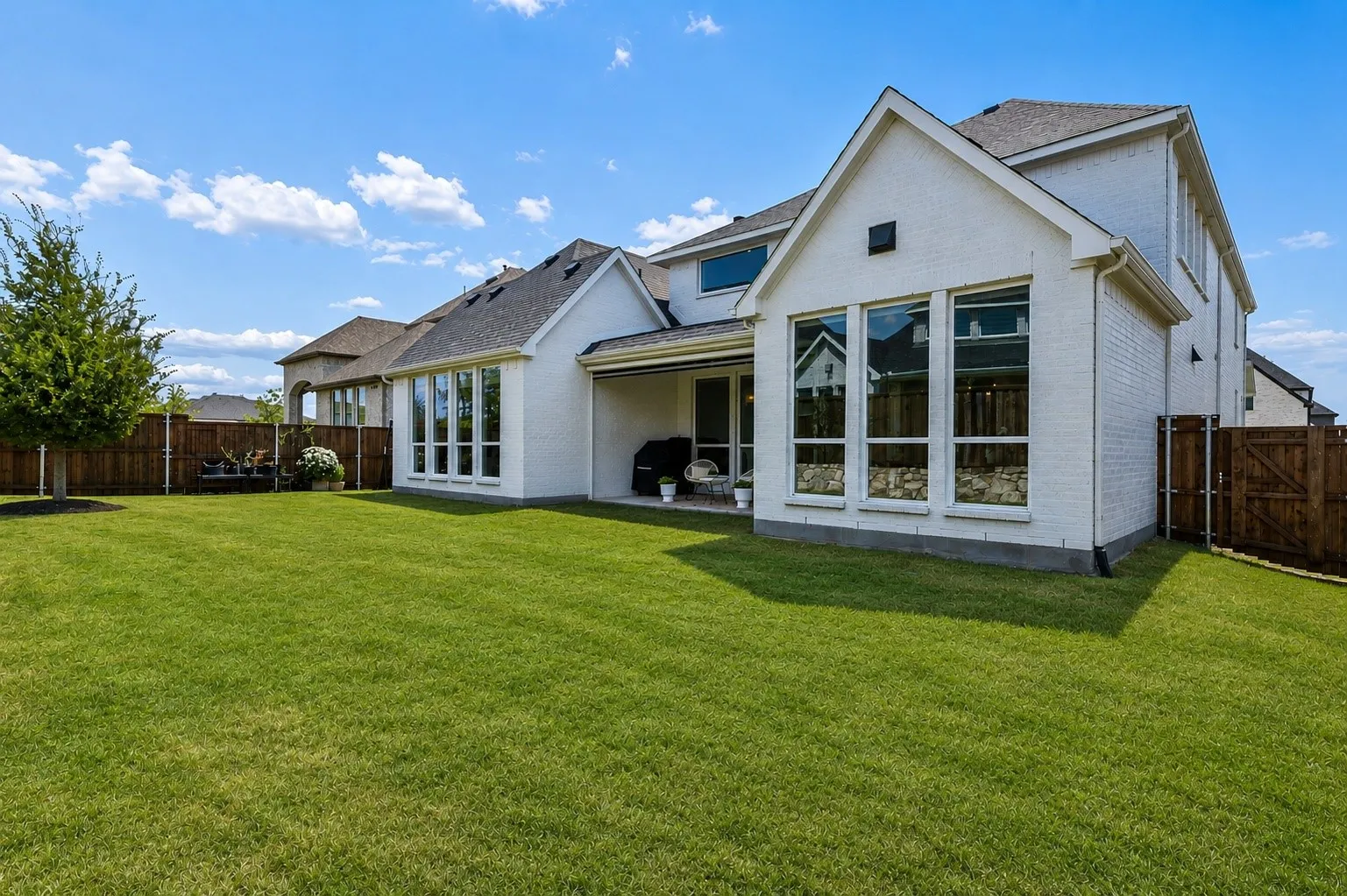 Expansive green lawn with a white brick exterior and a covered patio