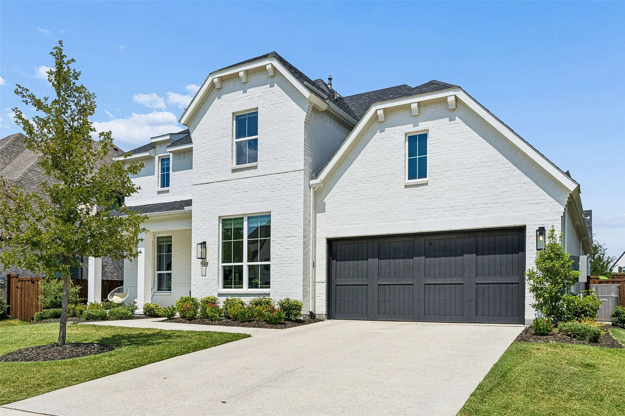 White brick exterior with dark trim windows, covered entry, attached garage with dark panel door, and concrete driveway