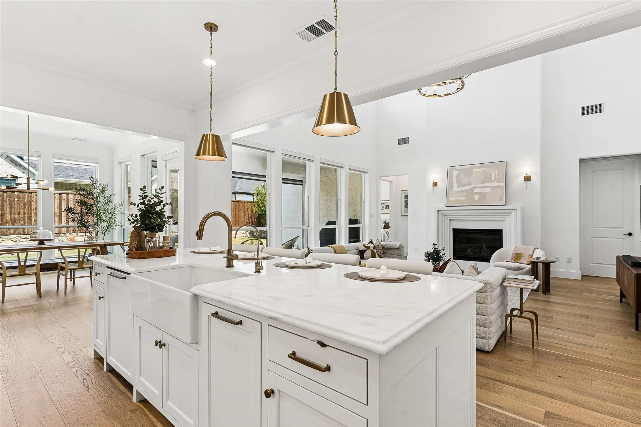 Kitchen island with white cabinetry, a farmhouse sink, and a brass-finish faucet, complemented by two brass-finish pendant lights