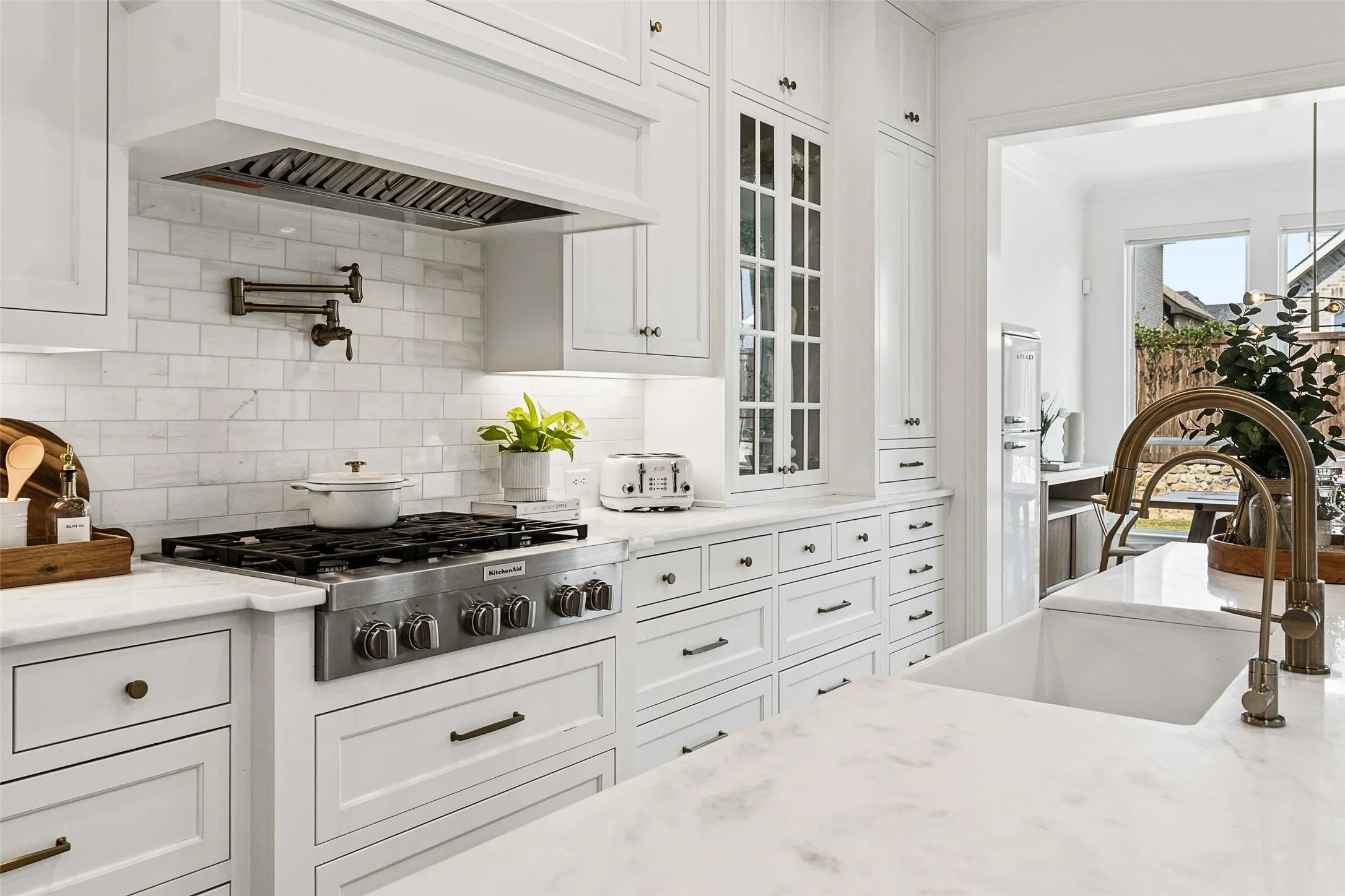 White cabinetry with dark hardware, stone countertops, subway tile backsplash, and a built-in range with a pot filler