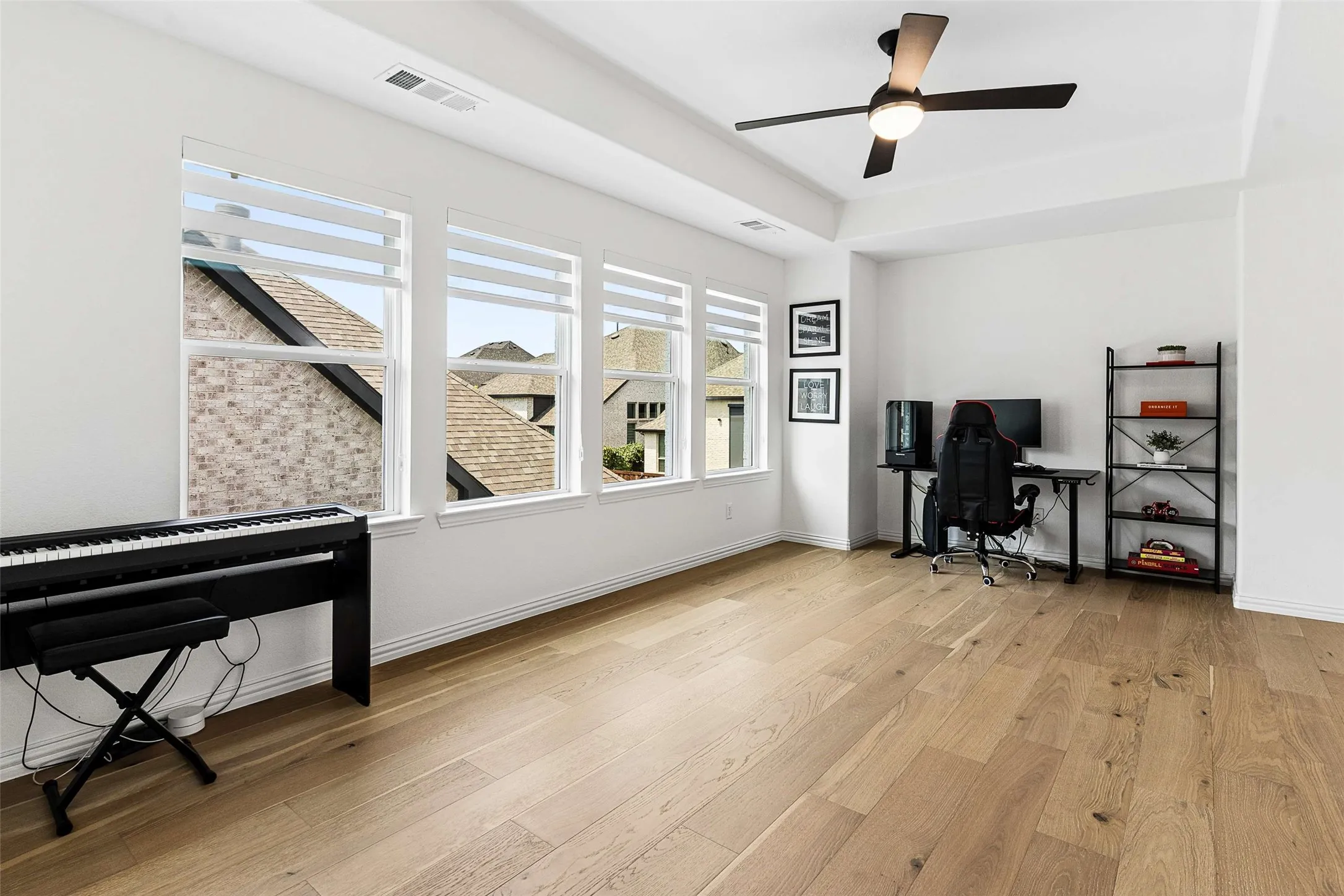 Light wood-finish flooring, recessed ceiling, modern ceiling fan, multiple windows, and white walls