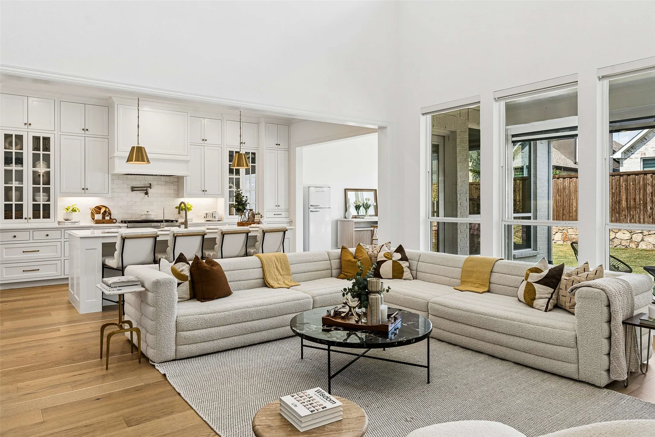 Open-concept living space featuring high ceilings, wood-finish flooring, a white kitchen with an island, and large windows
