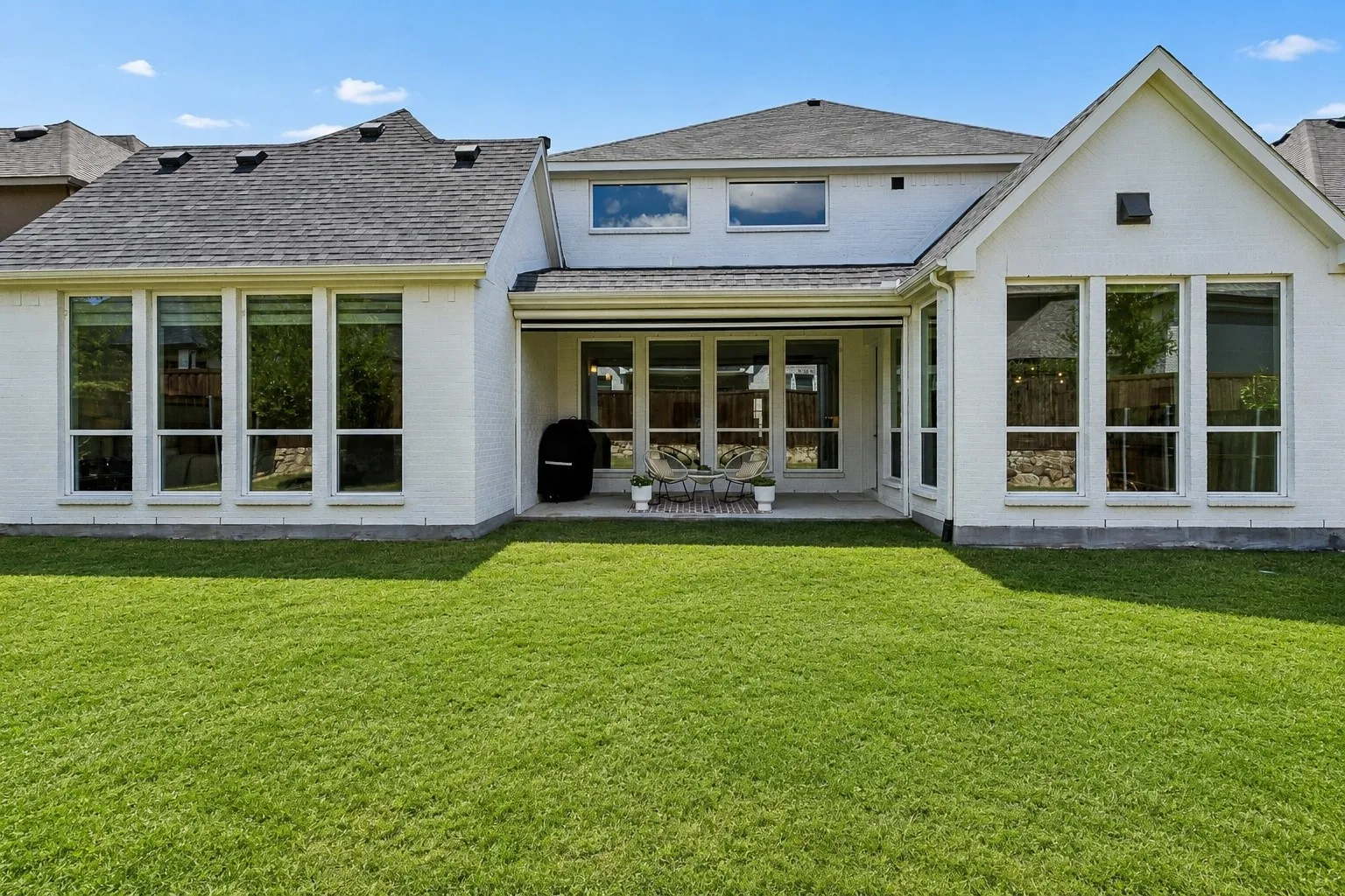 Expansive green lawn, brick exterior with white finish, multiple large windows, and a covered patio area