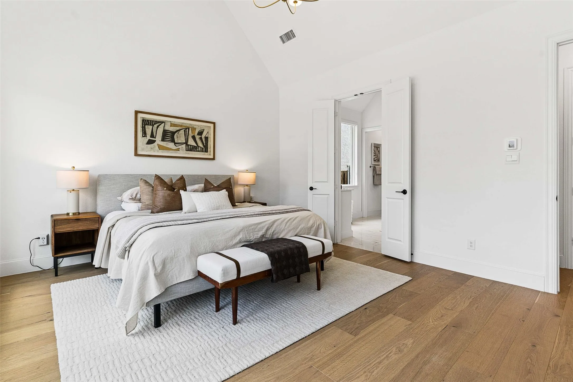 Vaulted ceiling with a contemporary light fixture, wide plank wood flooring, and white double doors